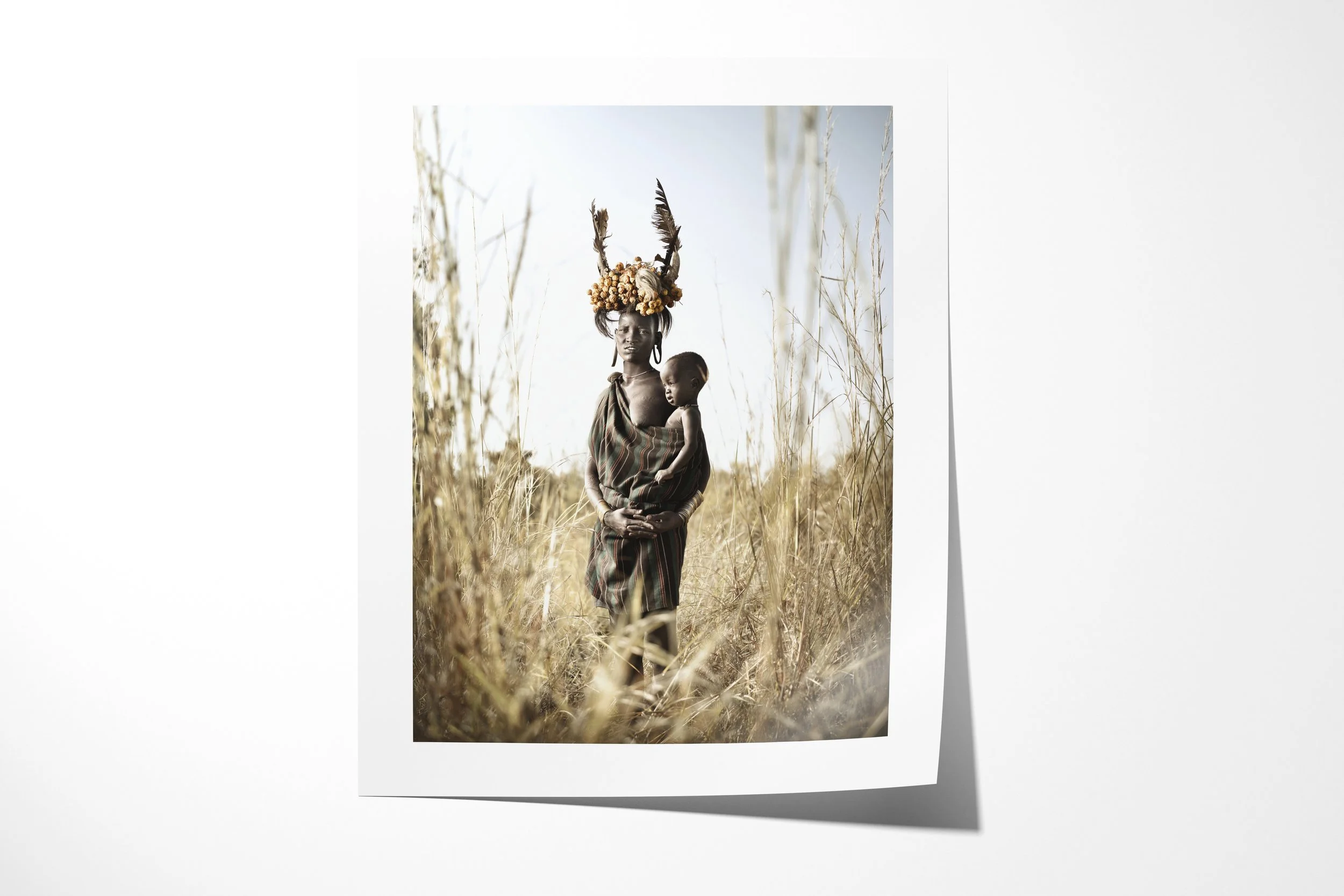 Fine art paper print of Chomeri & Dhada, showing a Mursi woman holding a child while wearing an elaborate headdress of horns, feathers and fruit.