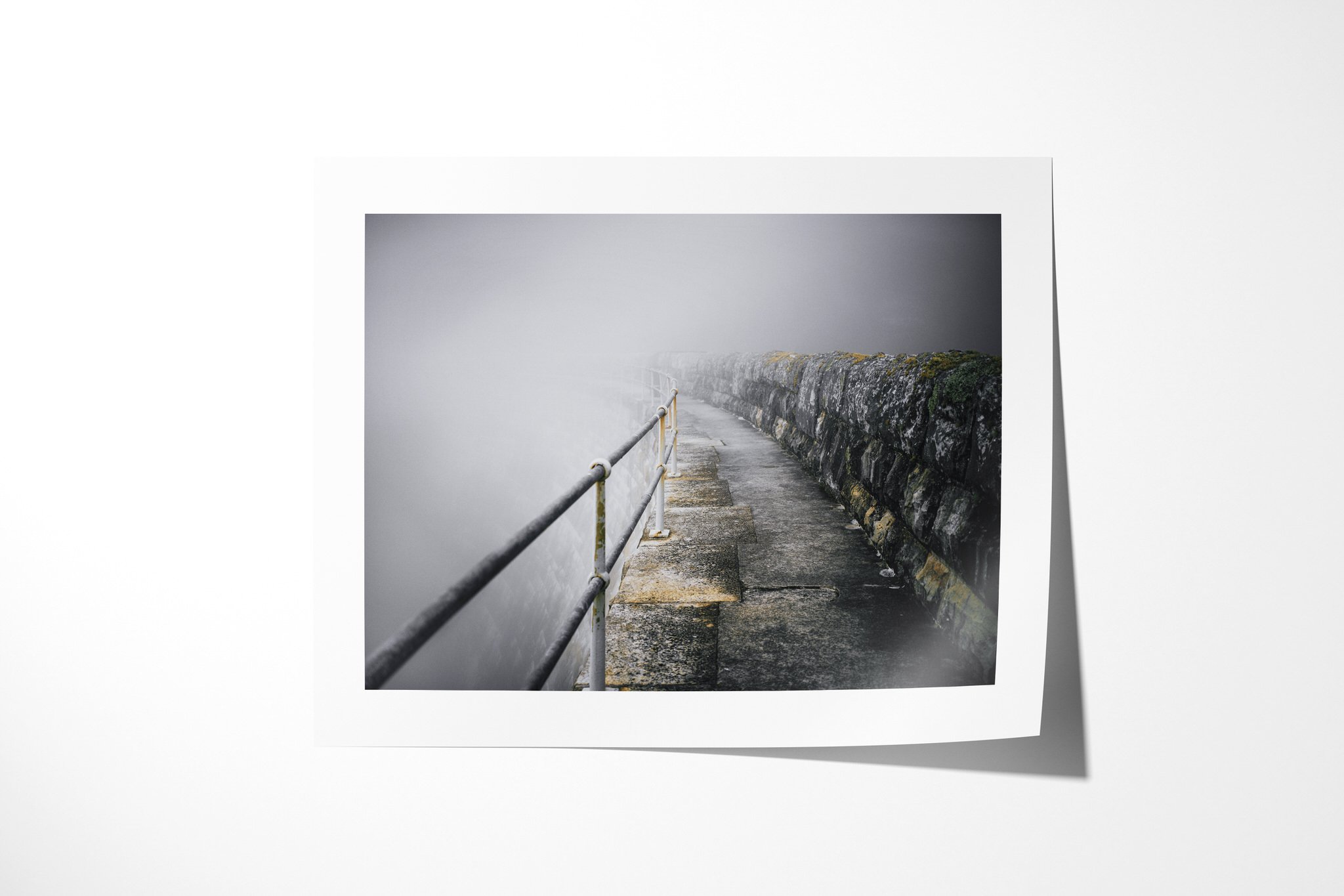 Fine art paper presentation of Ballustrade, depicting a weathered concrete walkway between a metal handrail and stone wall, curving out of sight into dense fog.