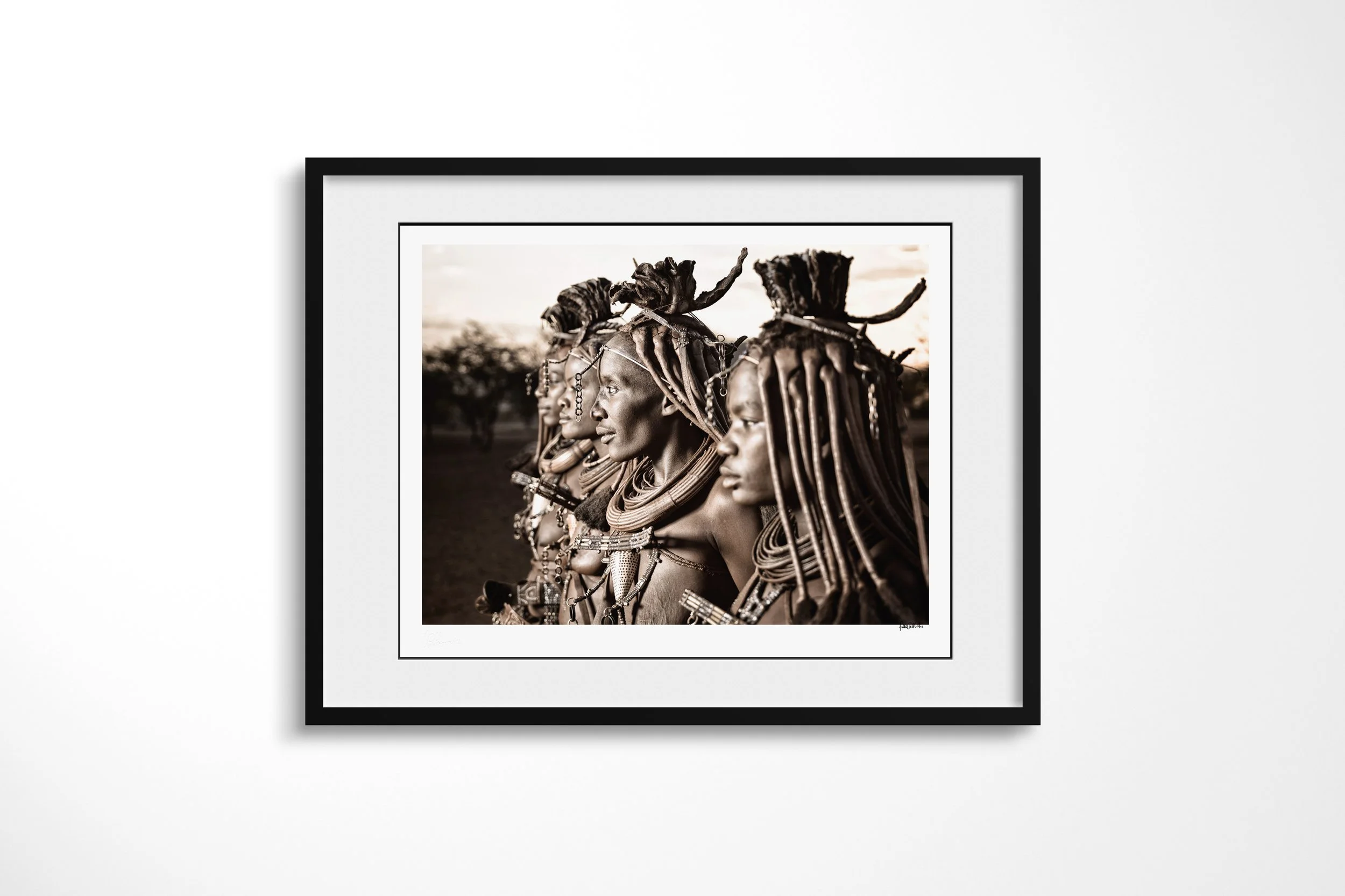 Framed presentation of Katitjii in a black frame and white mount, showing four Himba women shown in close profile, their otjize-dressed hair and jewellery overlapping across the frame.
