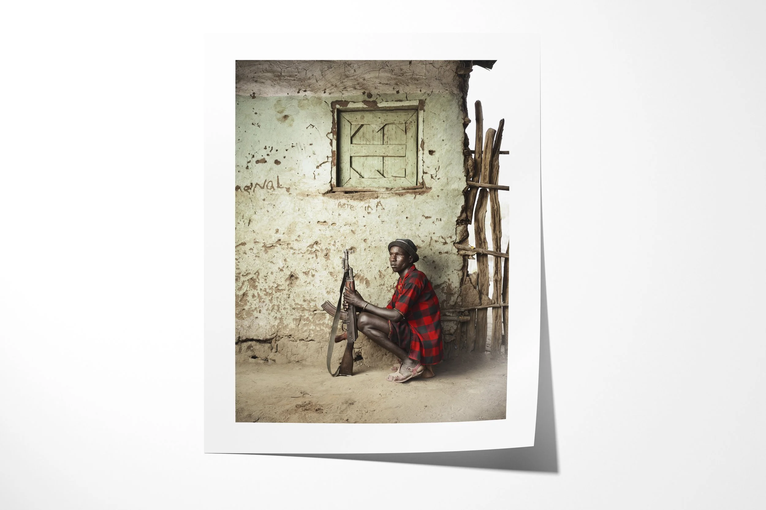 Fine art paper print of Hegere, showing an Arbore man seated on a low wooden headrest-stool with a rifle beside an earthen wall.