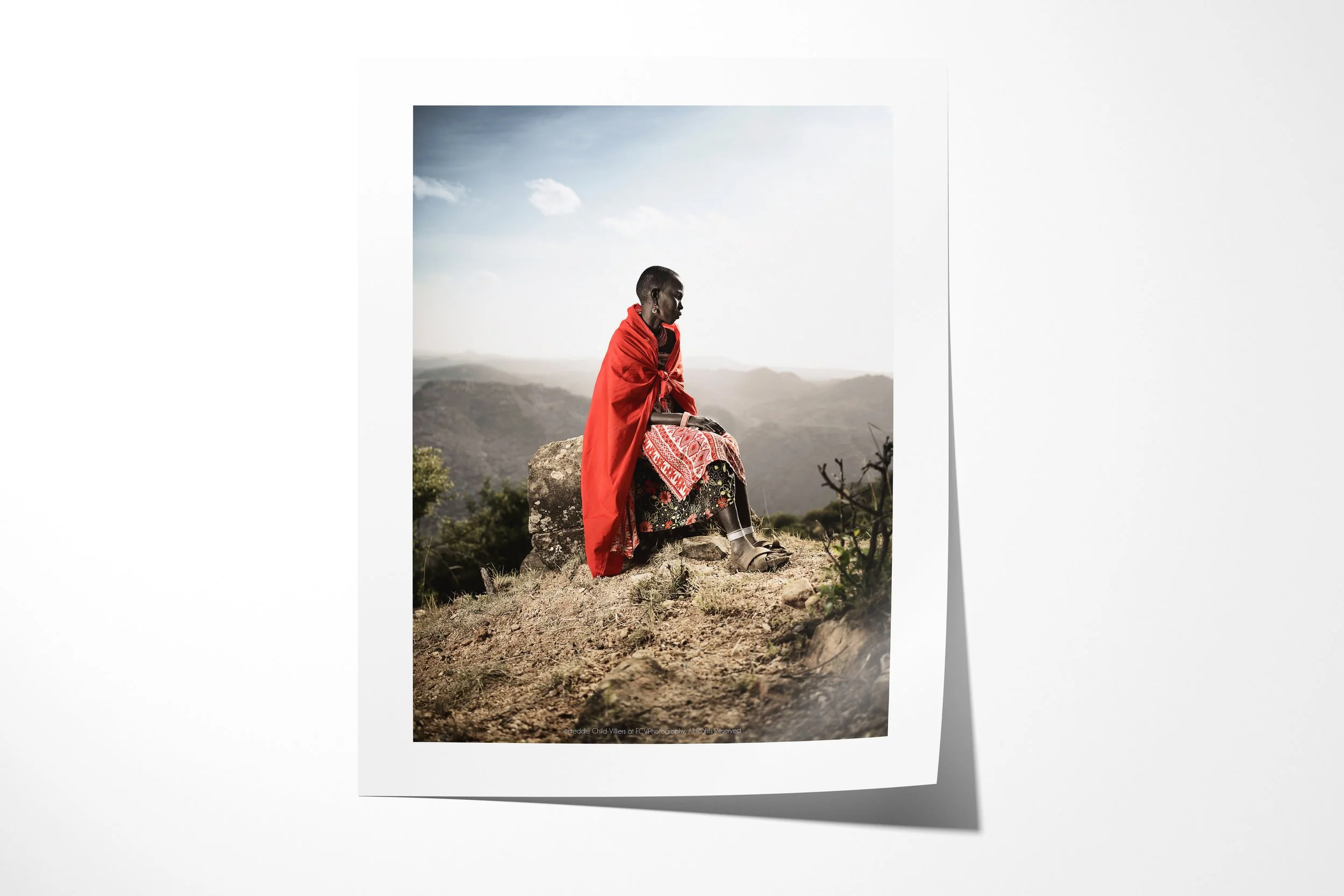Fine art paper print of Msari, showing a Samburu woman in a red wrap seated on a high rock above the Matthews Mountains.