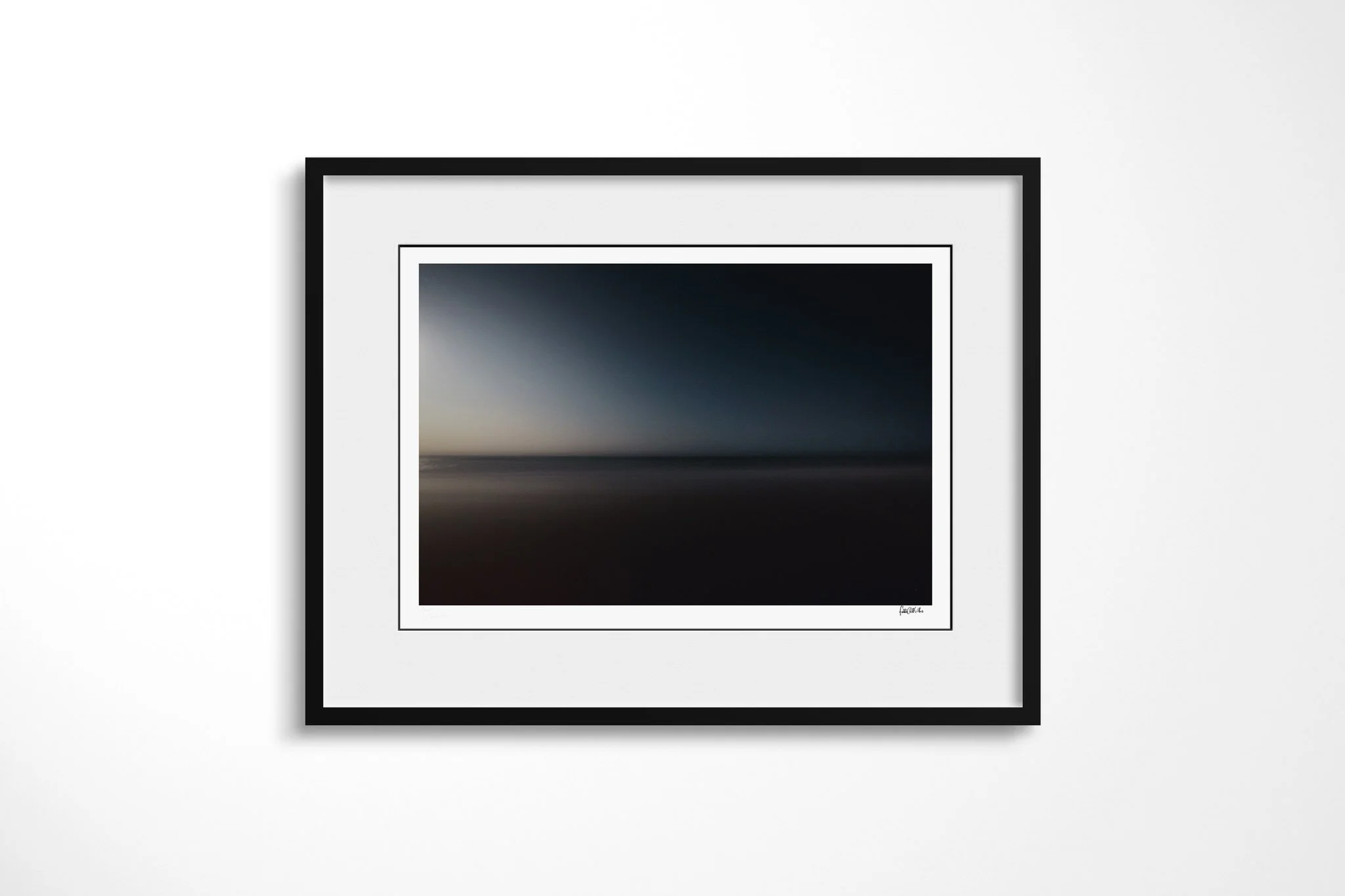 Framed fine art presentation of Outlook in a black frame with a white mount, depicting soft, nearly abstract bands of dark blue sky, muted sea and reddish foreground divided by a faint horizon.