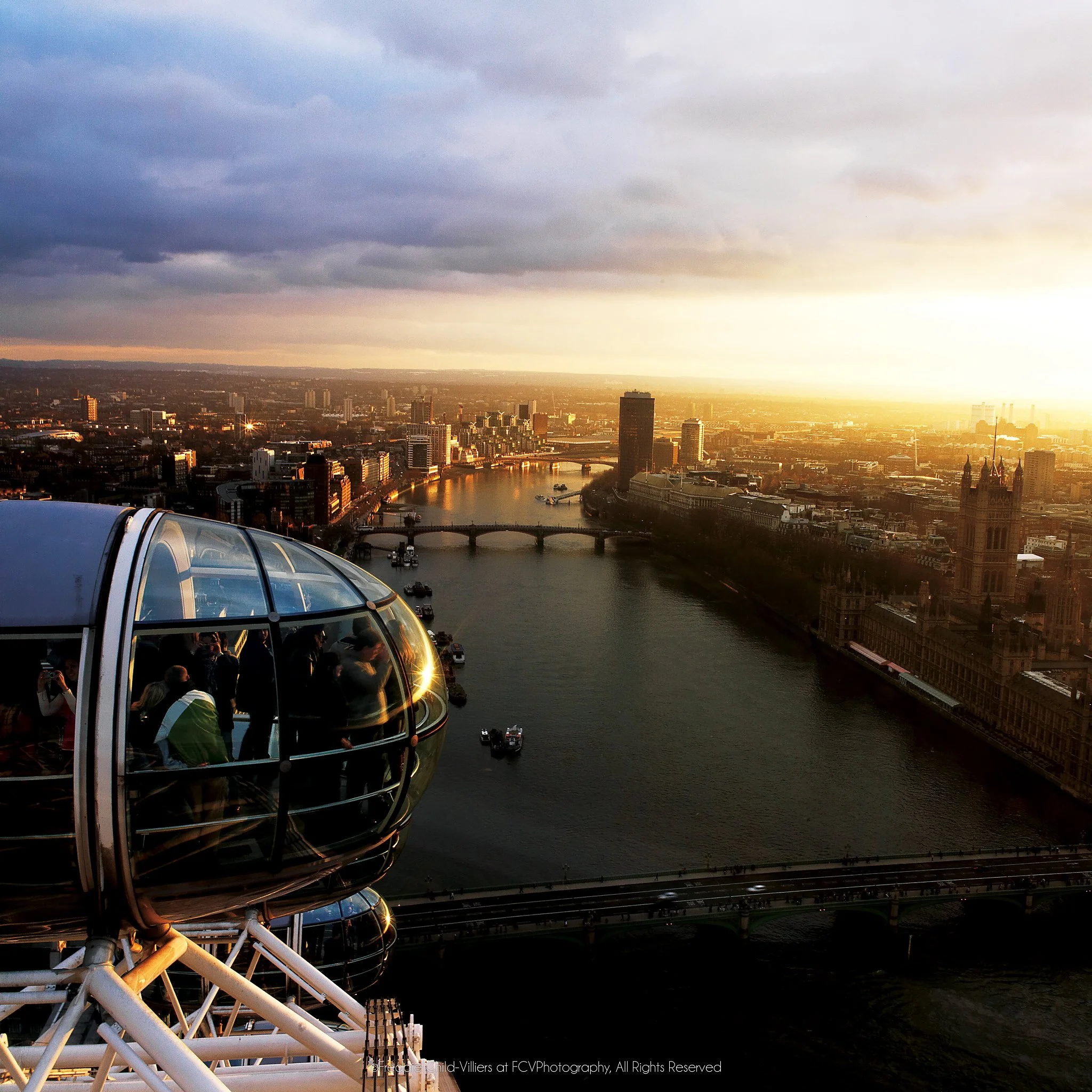 London Eye capsules above the River Thames, Westminster Bridge and the Houses of Parliament at sunset.