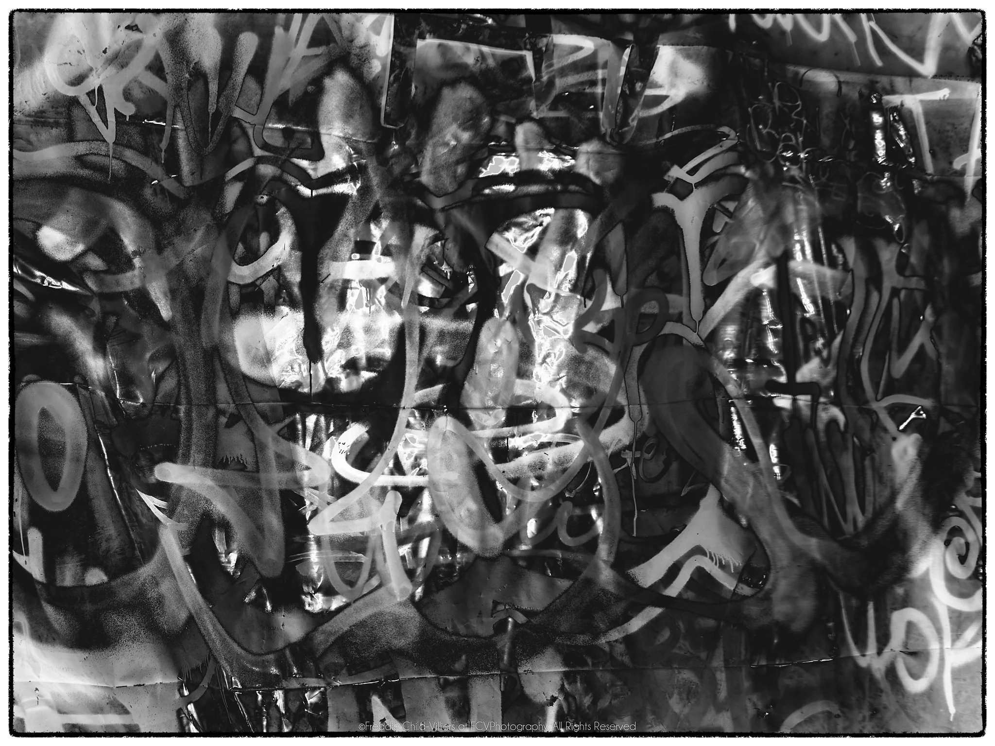 Layered monochrome surface of looping graffiti-like marks, seams, reflections and partially recognisable figures.