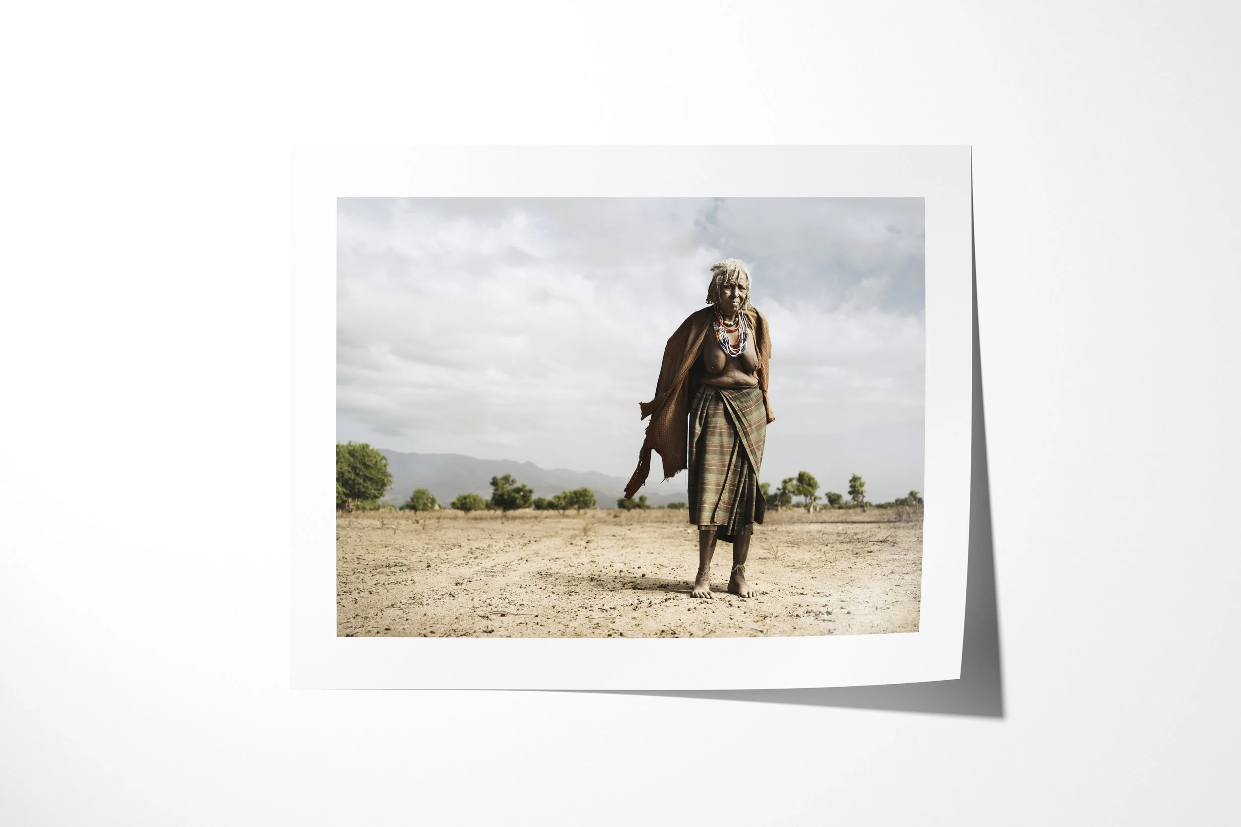 Fine art paper print of Rufa, showing an older Arbore woman in layered beadwork and wrapped clothing standing on a dry plain.