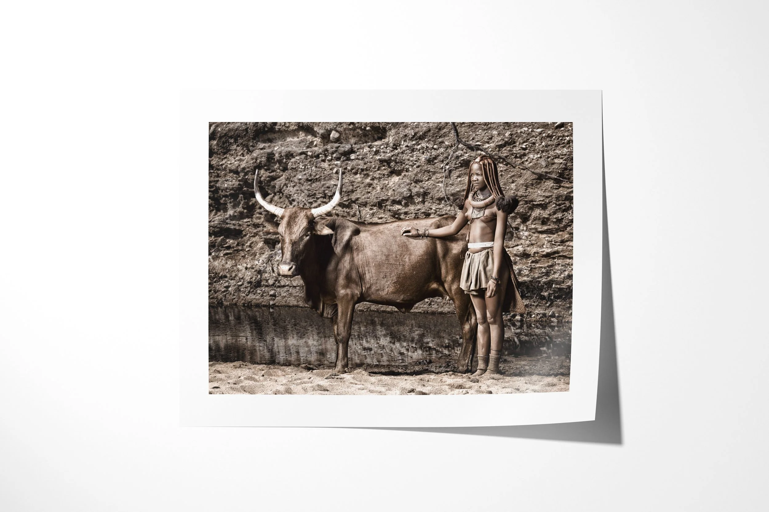 Fine art paper print of MBunengo, showing MBunengo standing beside a Nguni bull at a watering hole.