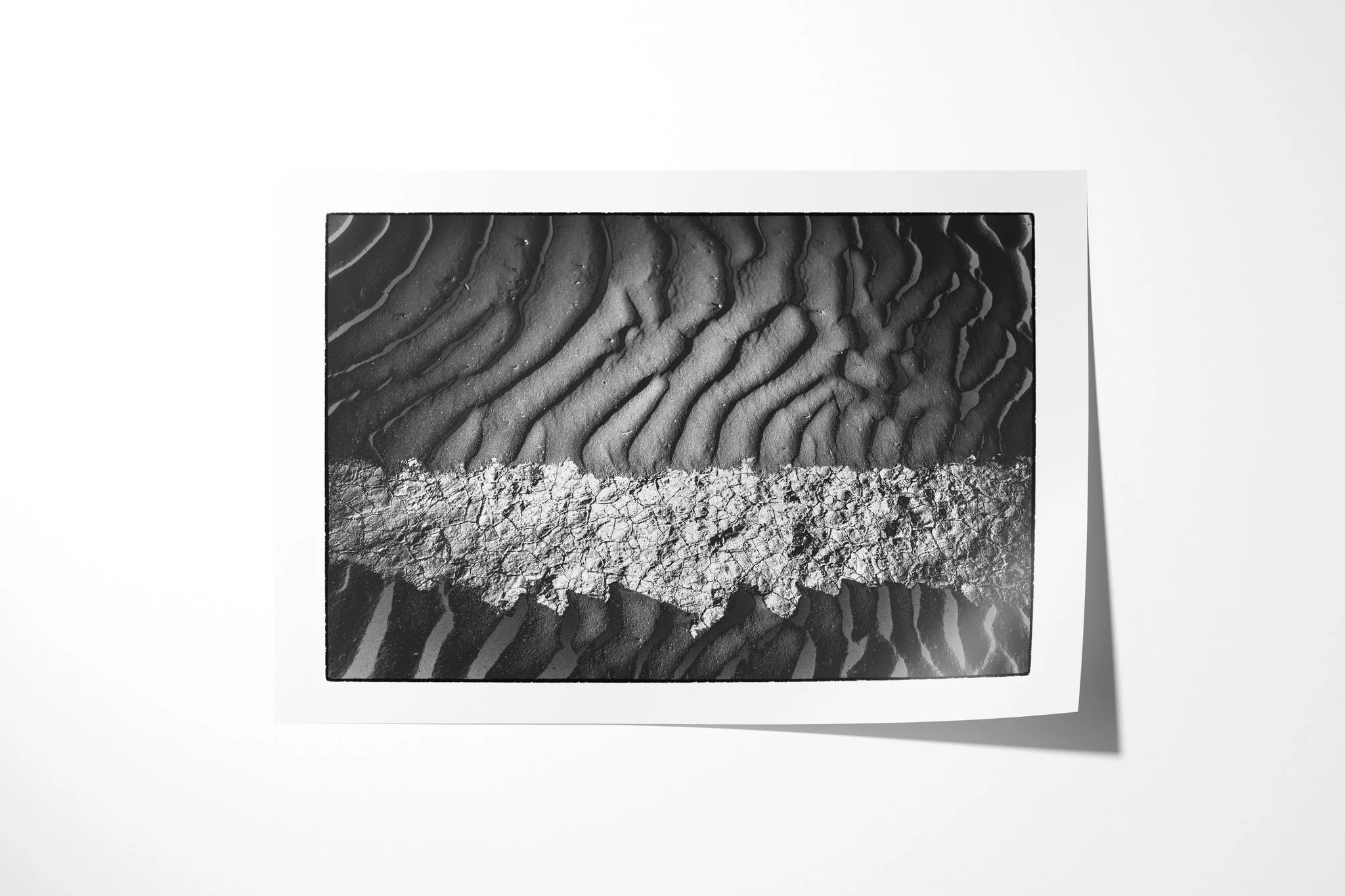Khamsin II presented as an unframed fine art paper print, showing a pale cracked band crossing dark rippled sand in a high-contrast horizontal composition.