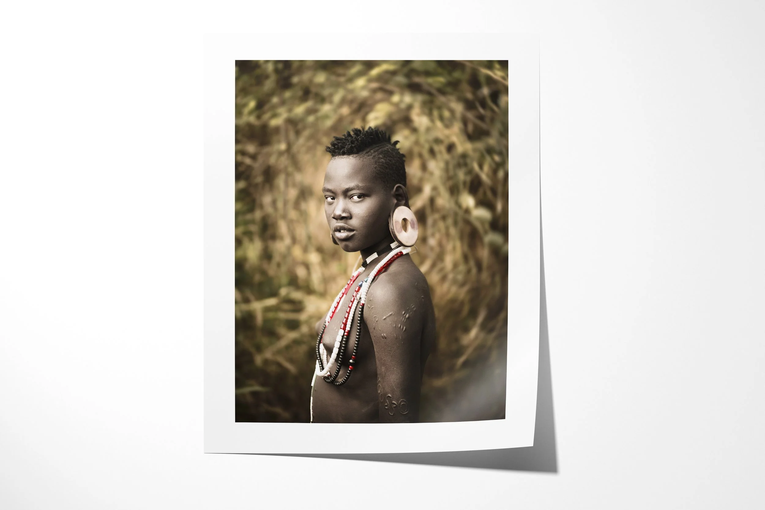 Fine art paper print of Kernahoir, showing a young Mursi girl in profile with a large ear disc, bead necklaces and scarification on her shoulder.