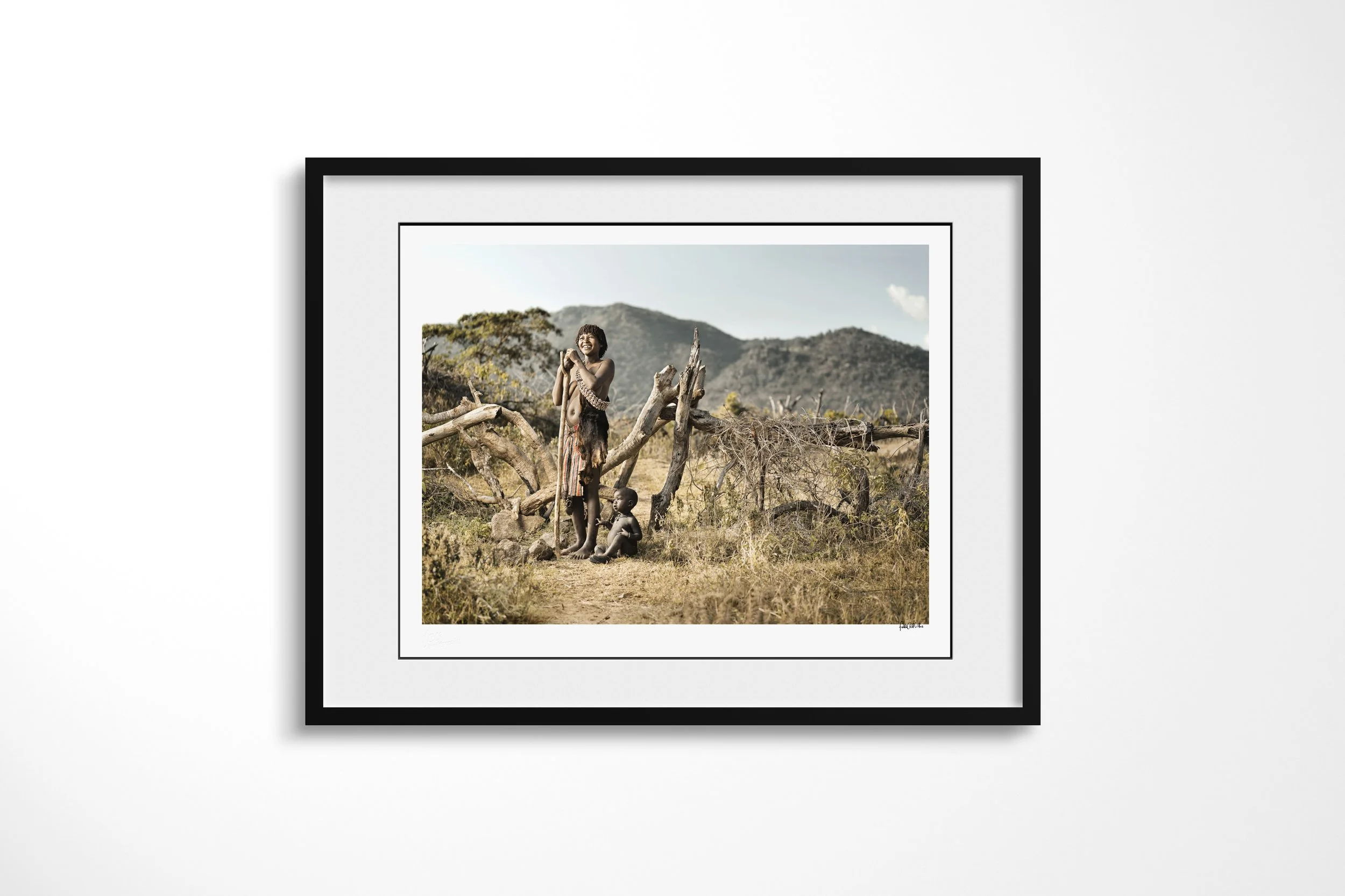 Framed presentation of Sani & Mito in a black frame and white mount, showing a Banna mother standing with a child beneath a tree while another child sits beside her.