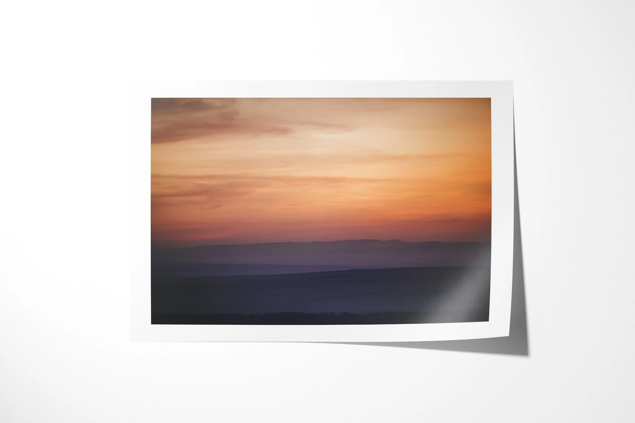 Fine art paper presentation of Sunrise, depicting soft horizontal bands of salmon, orange and mauve above blurred dark hills at sunrise.