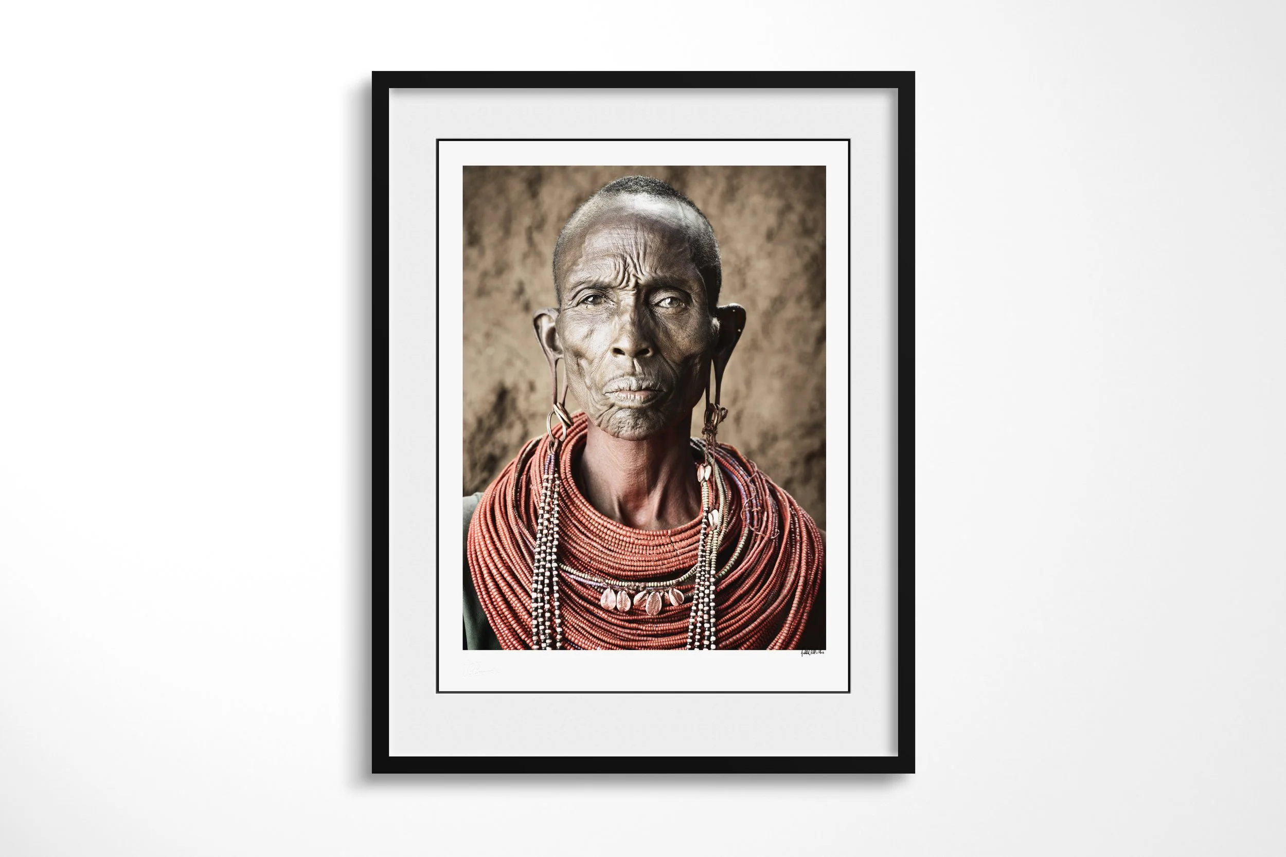 Framed presentation of Nalary - “The Mother of Warriors” in a black frame and white mount, showing a close portrait of a Samburu mother wearing ochre, layered beadwork and paired ear ornaments.