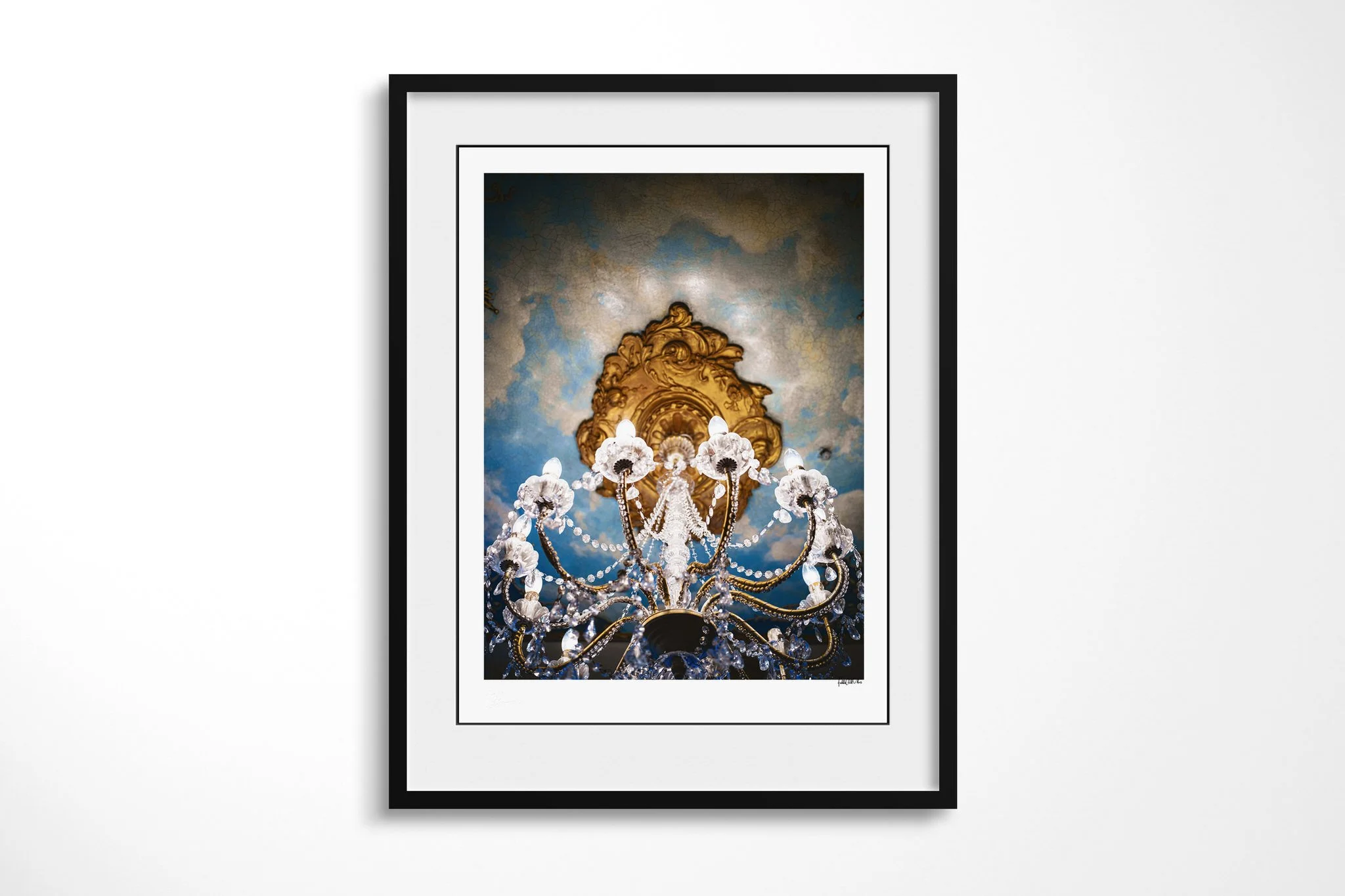 Chandelier presented in a black frame with a white mount, depicting an ornate crystal chandelier viewed from below against a gilded ceiling rose and cracked blue plaster.