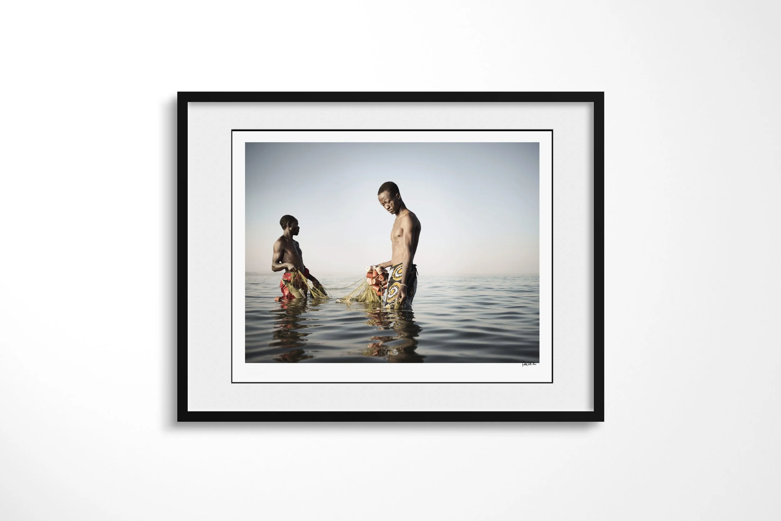 Framed presentation of Jeremy & Zacheus in a black frame and white mount, showing two El Molo fishermen wading in Lake Turkana as they retrieve a net.