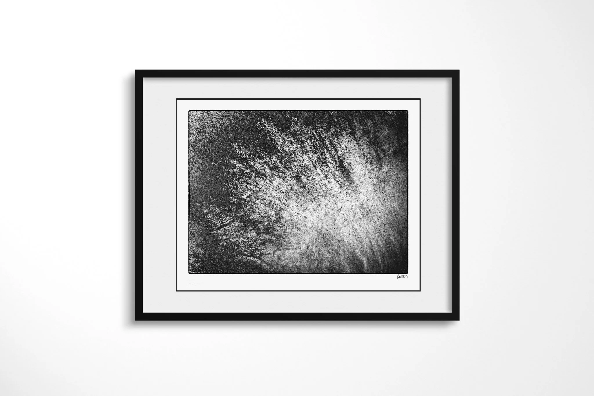 Black-framed presentation of Manganese II with a wide white mount, featuring a bright fan of fine radiating streaks spreading diagonally across a dark granular surface.