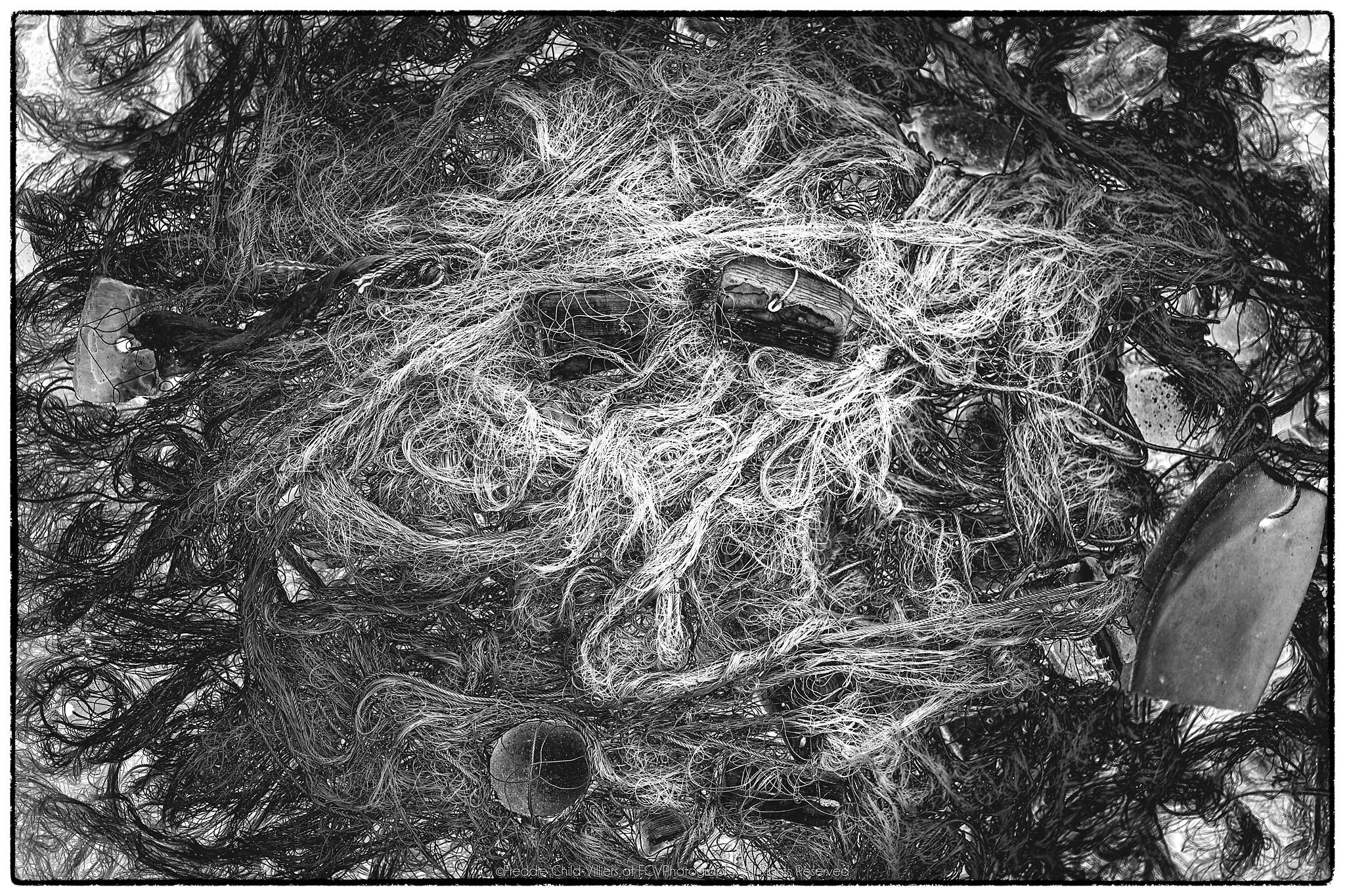 Dense tangle of netting, fine cord, rope and scattered weathered fragments in black and white.