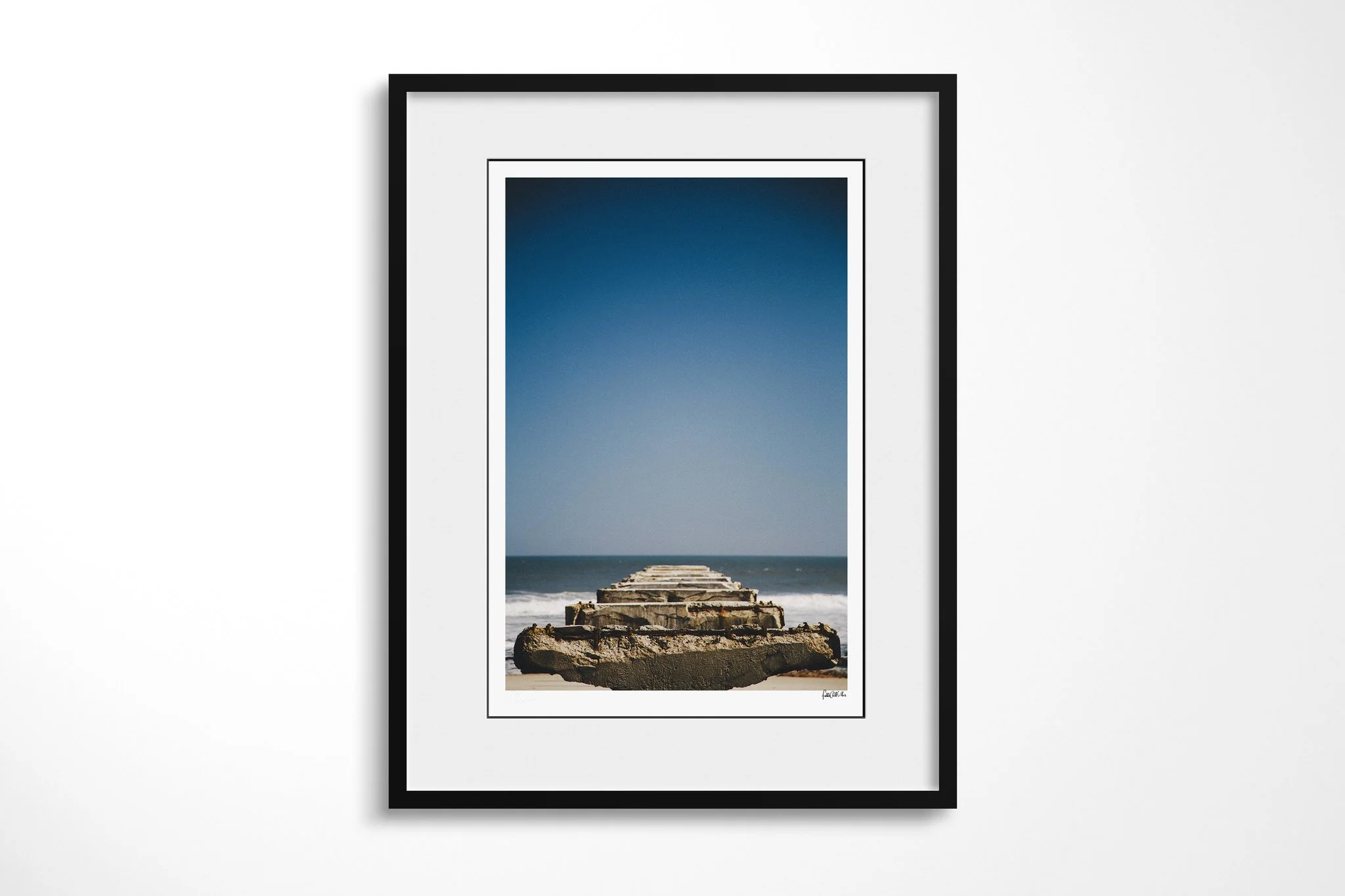 Black-framed fine art print of Skeleton Coast with a white mount, showing crumbling concrete remnants extending from sand into the Atlantic surf on Namibia's Skeleton Coast.