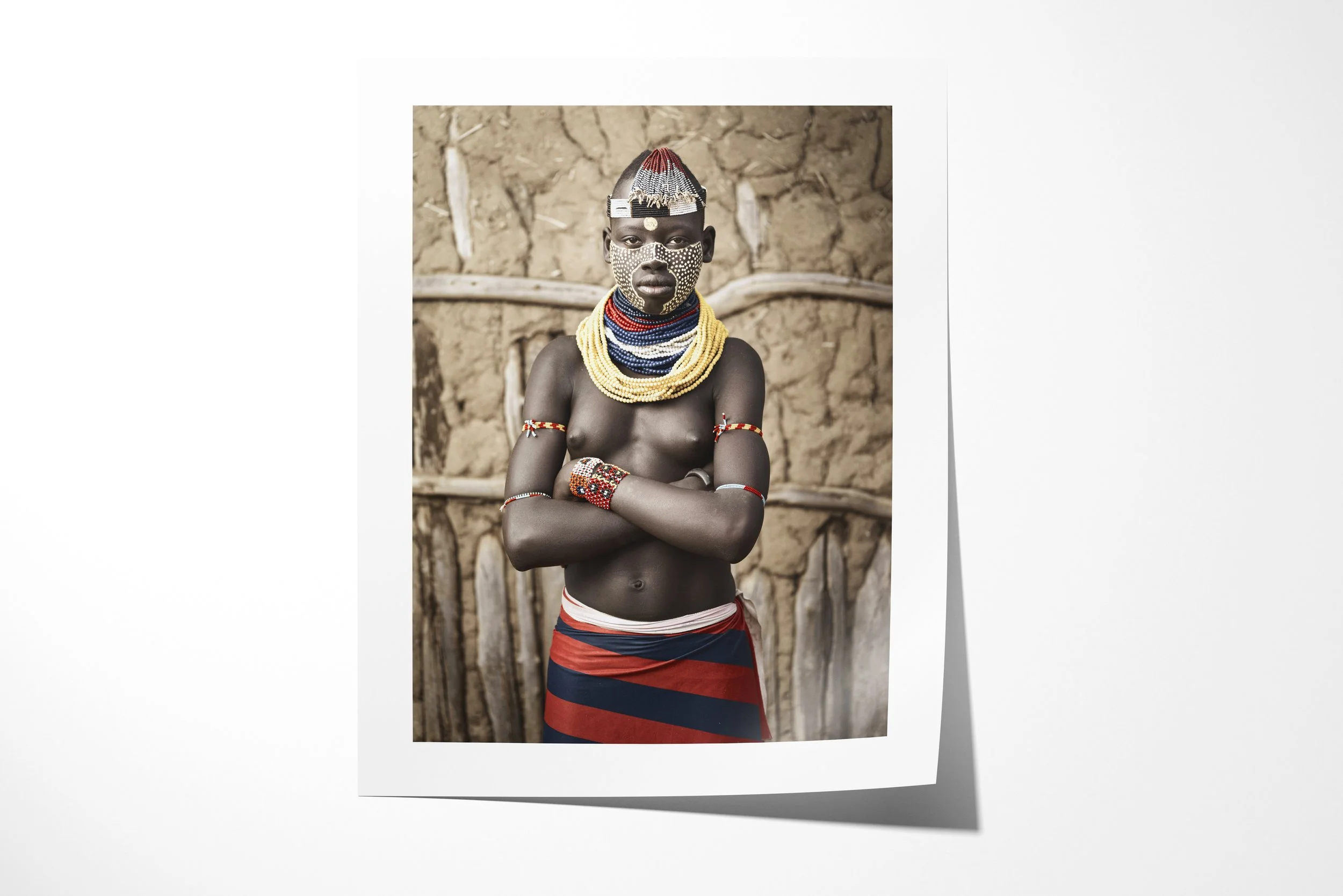 Fine art paper print of Tena, showing a Kara woman with patterned facial paint, layered beadwork and folded arms before an earthen wall.