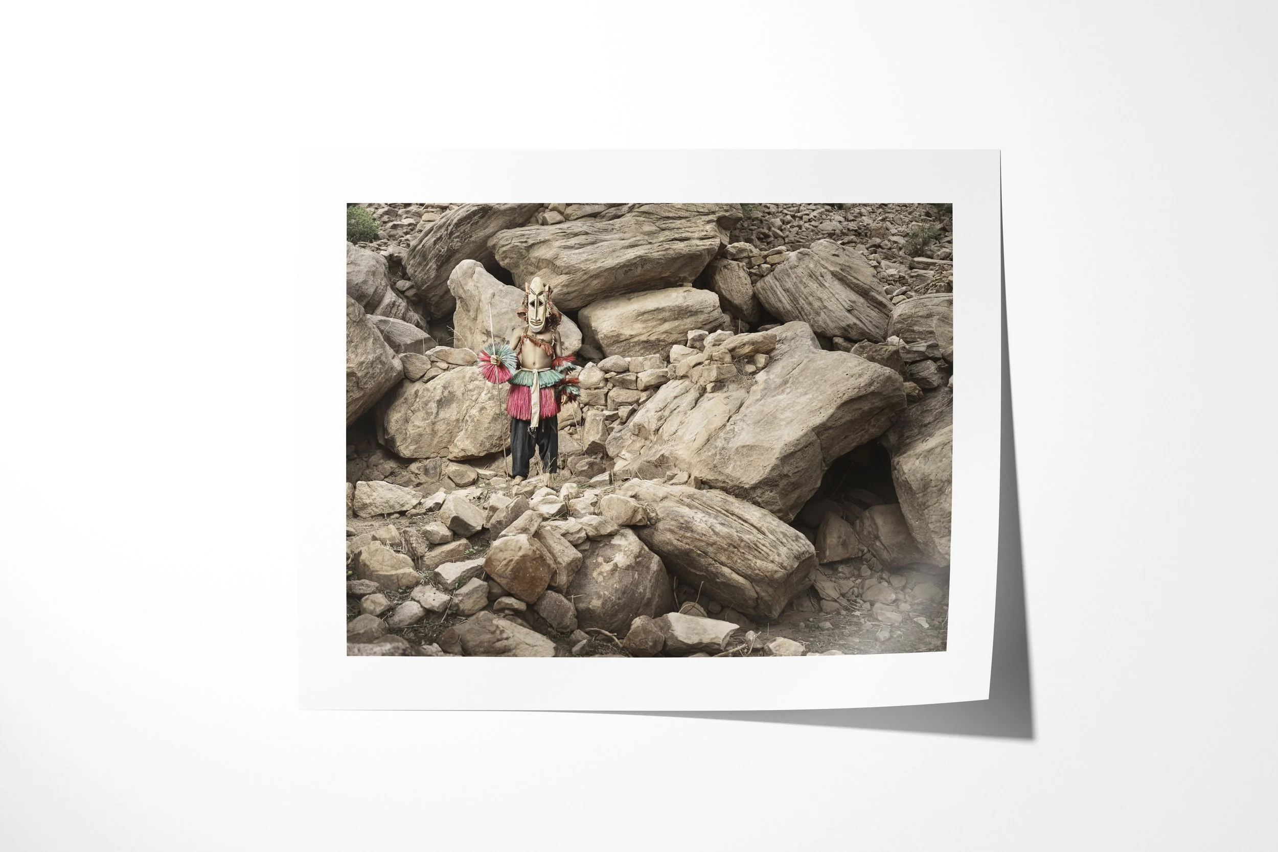 Fine art paper print of Djon (Mask), showing a Dogon antelope mask standing amid collapsed boulders and stone walls.