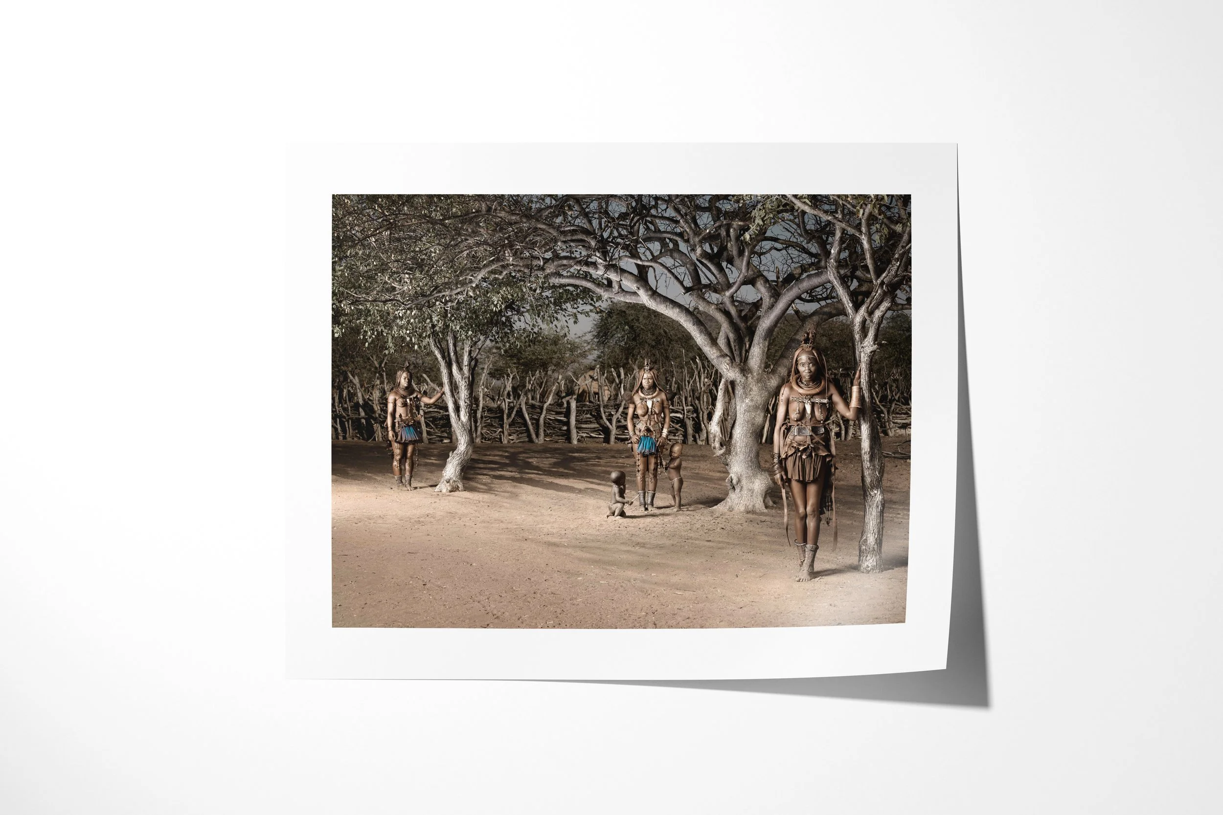 Fine art paper print of Waruakawa (left), Twahenwa (middle) and Katitjii (right), showing three Himba women and children spaced beneath a large tree within their homestead.
