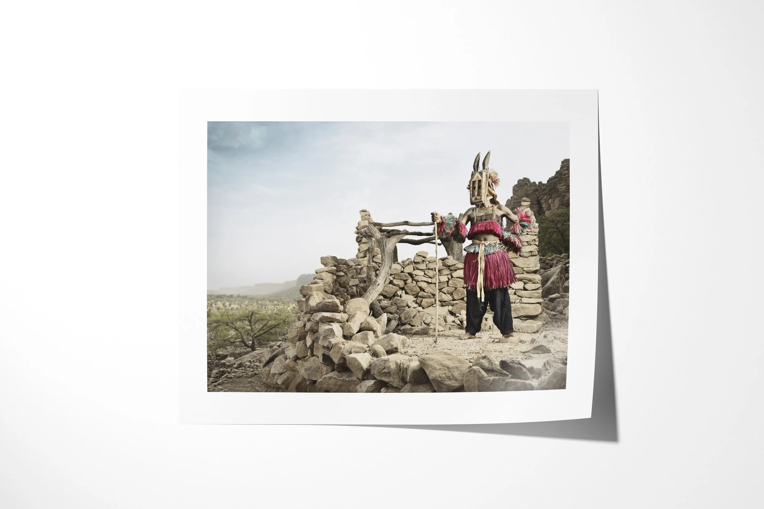 Fine art paper print of Walu (Mask) II, showing a Dogon Walu mask holding a staff among the stone walls of a cliff village.