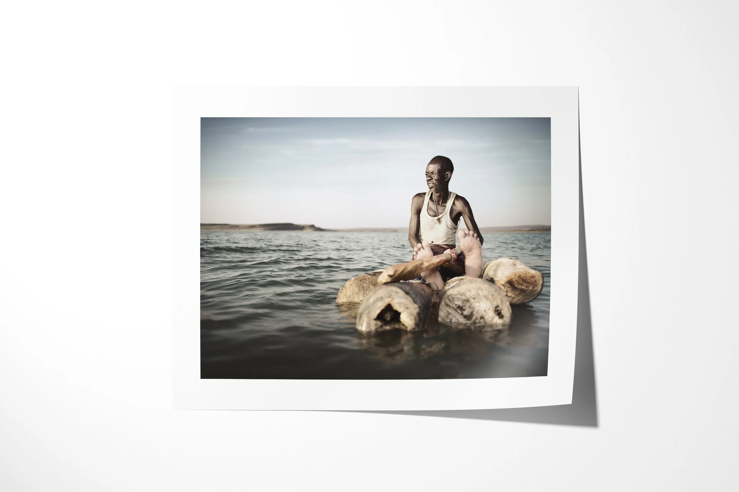 Fine art paper print of Lengutuk II, showing an El Molo fisherman seated on a raft of lashed palm logs on Lake Turkana.