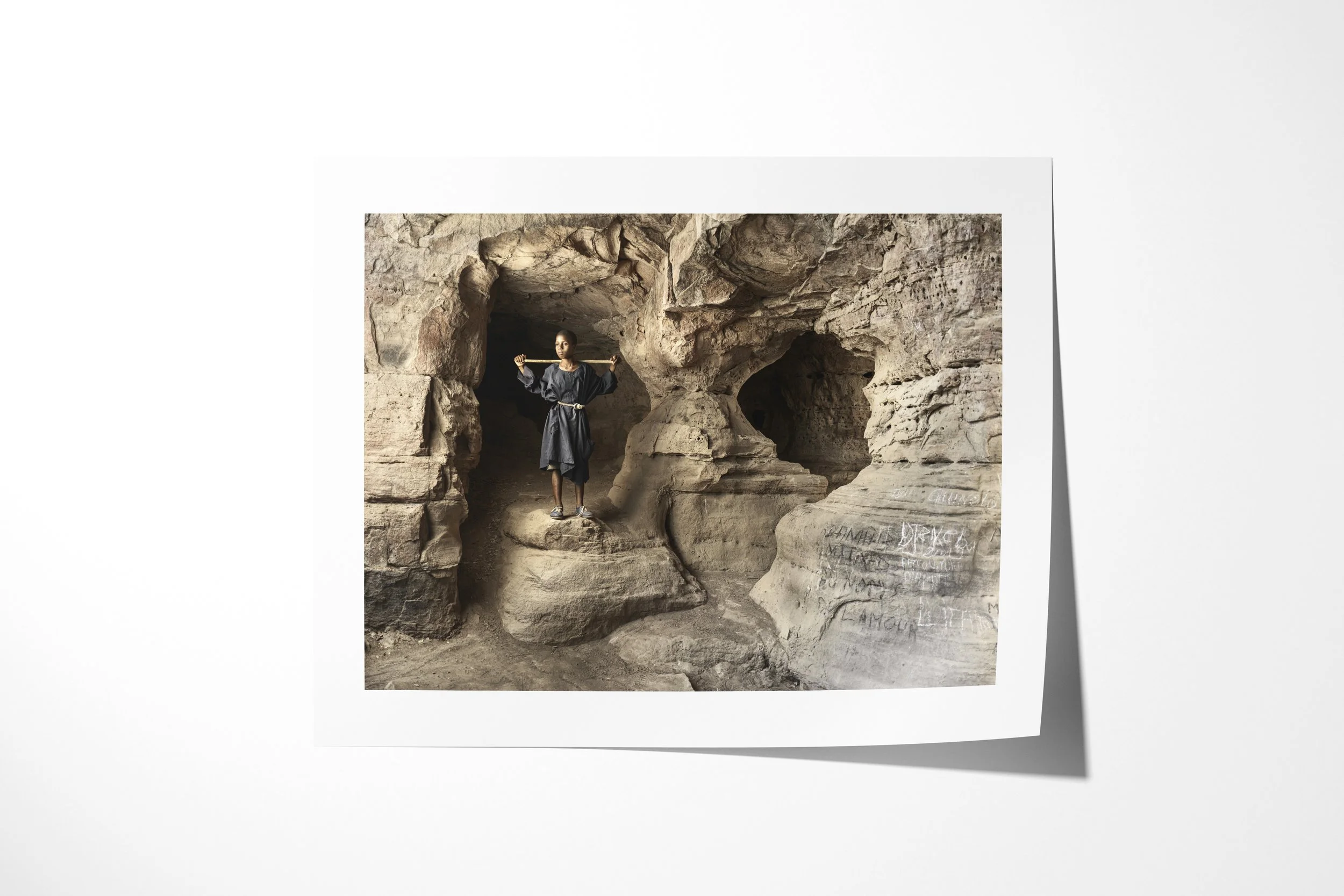 Fine art paper print of Modibo, showing Modibo standing with outstretched arms inside a cave marked with handwritten requests.
