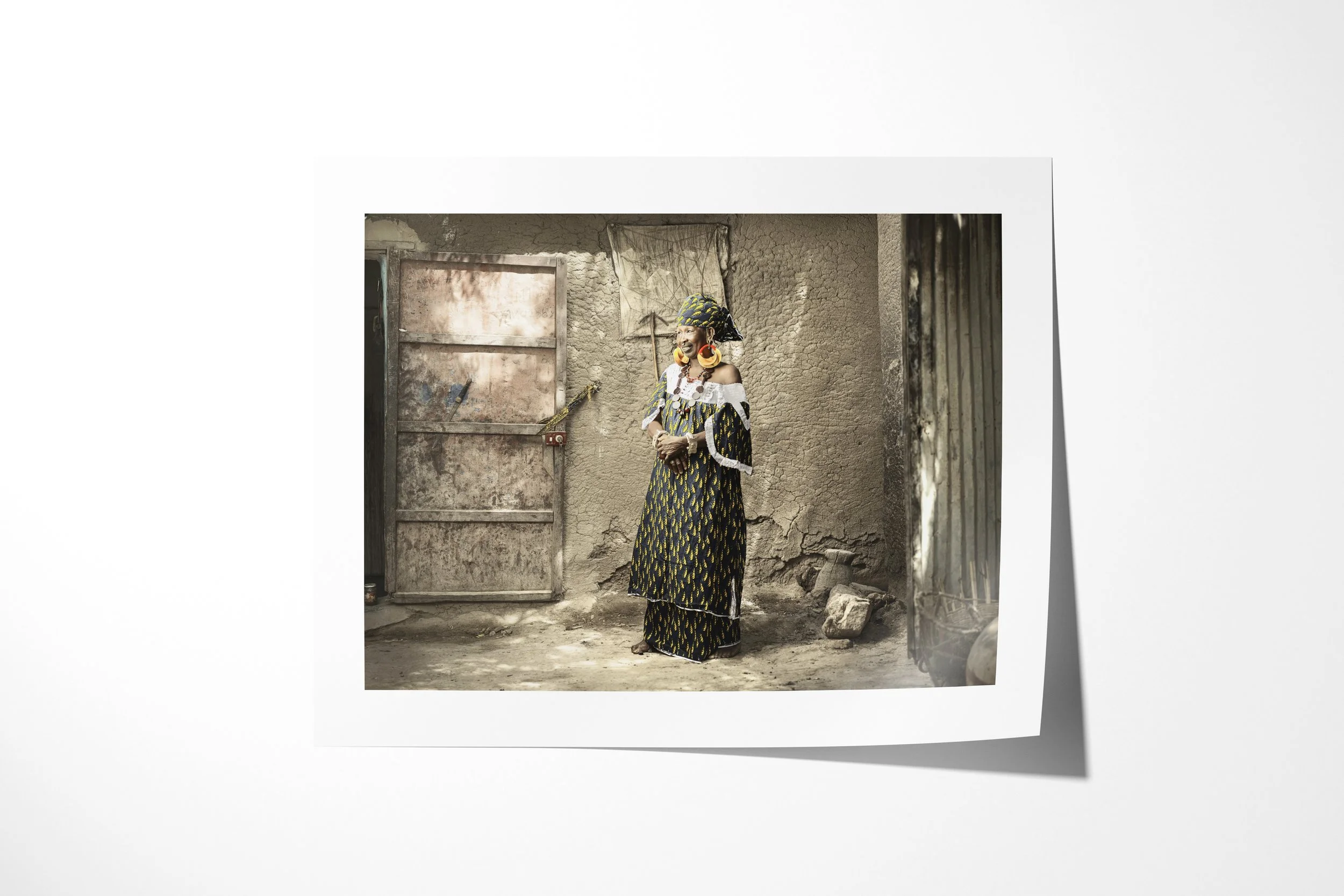 Fine art paper print of Thindel, showing Thindel wearing large gold earrings and patterned clothing beside a weathered metal door.