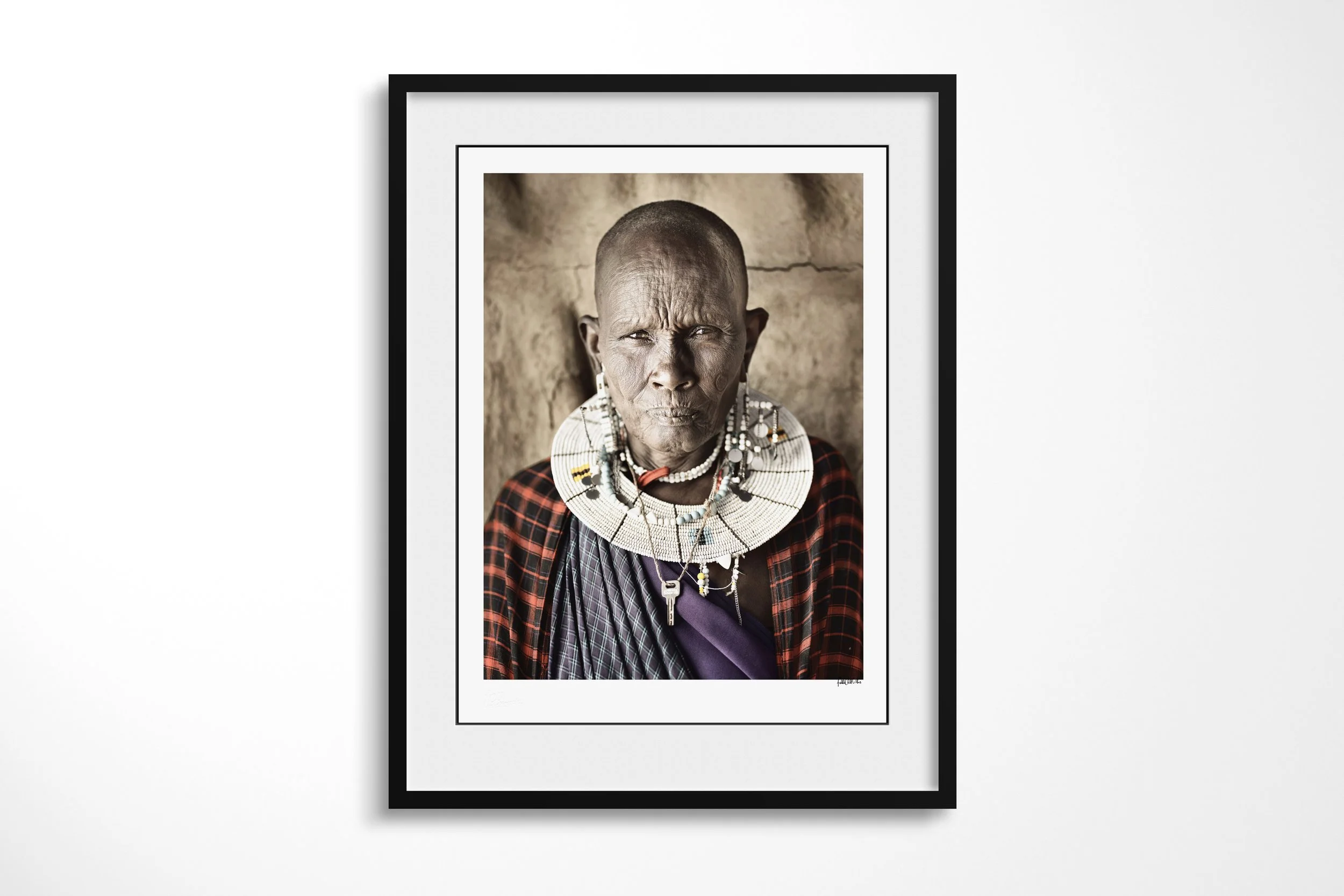 Framed presentation of Naleku in a black frame and white mount, showing a close portrait of a Maasai elder wearing a white bead collar and checked cloth.