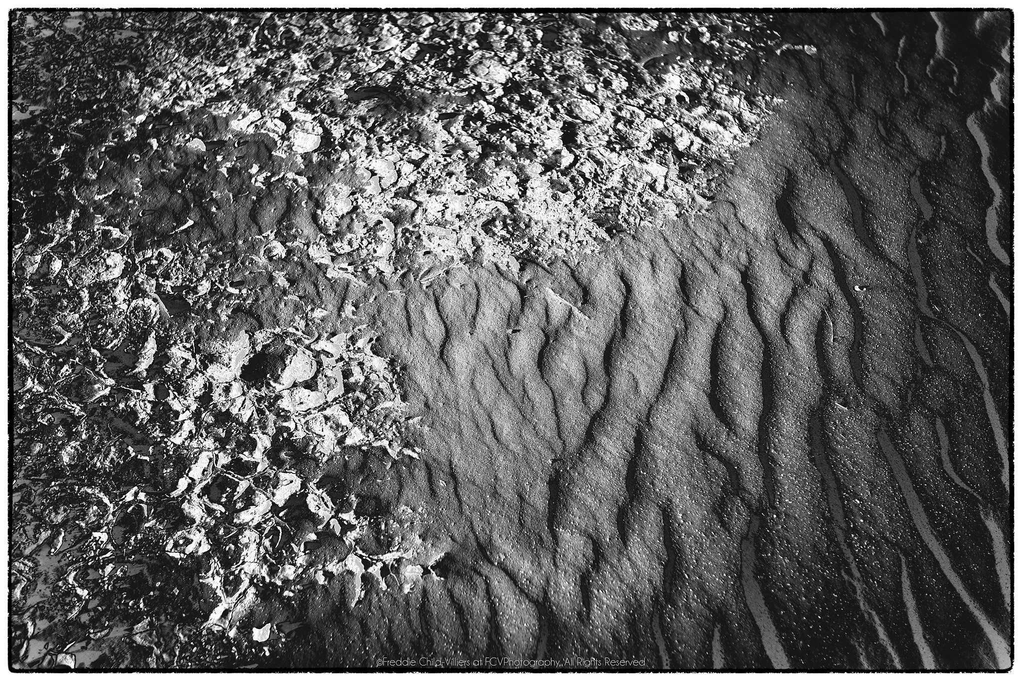 Broken granular crust meeting smoother rippled sand along an irregular curved boundary.