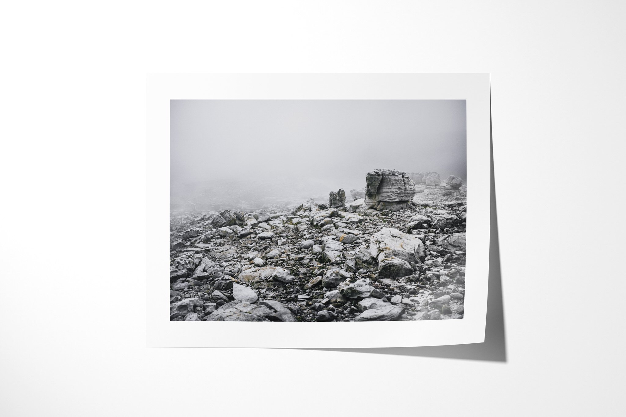 Unframed fine art paper print of Atmosphere, showing weathered boulders and broken rock fading into dense mist across a pale mountain landscape.