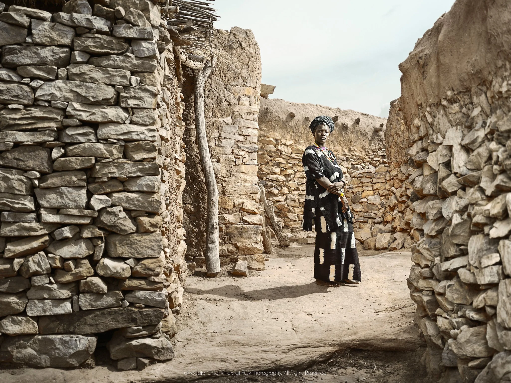 Yakoto standing in a narrow stone passage between the walls of a Dogon village.