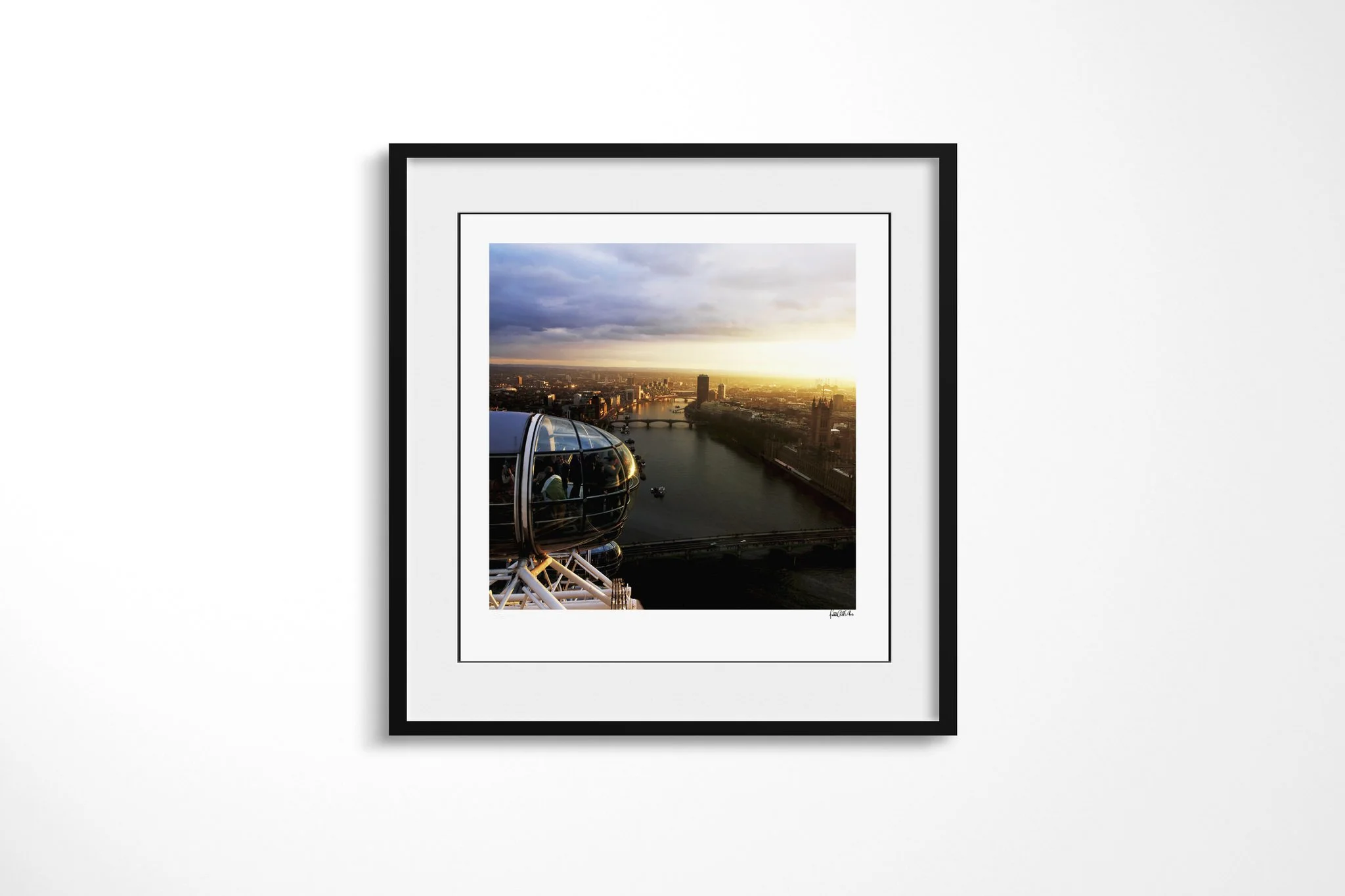 Framed presentation of Eye In The Sky in a black frame and white mount, showing London Eye capsules above the River Thames, Westminster Bridge and the Houses of Parliament at sunset.