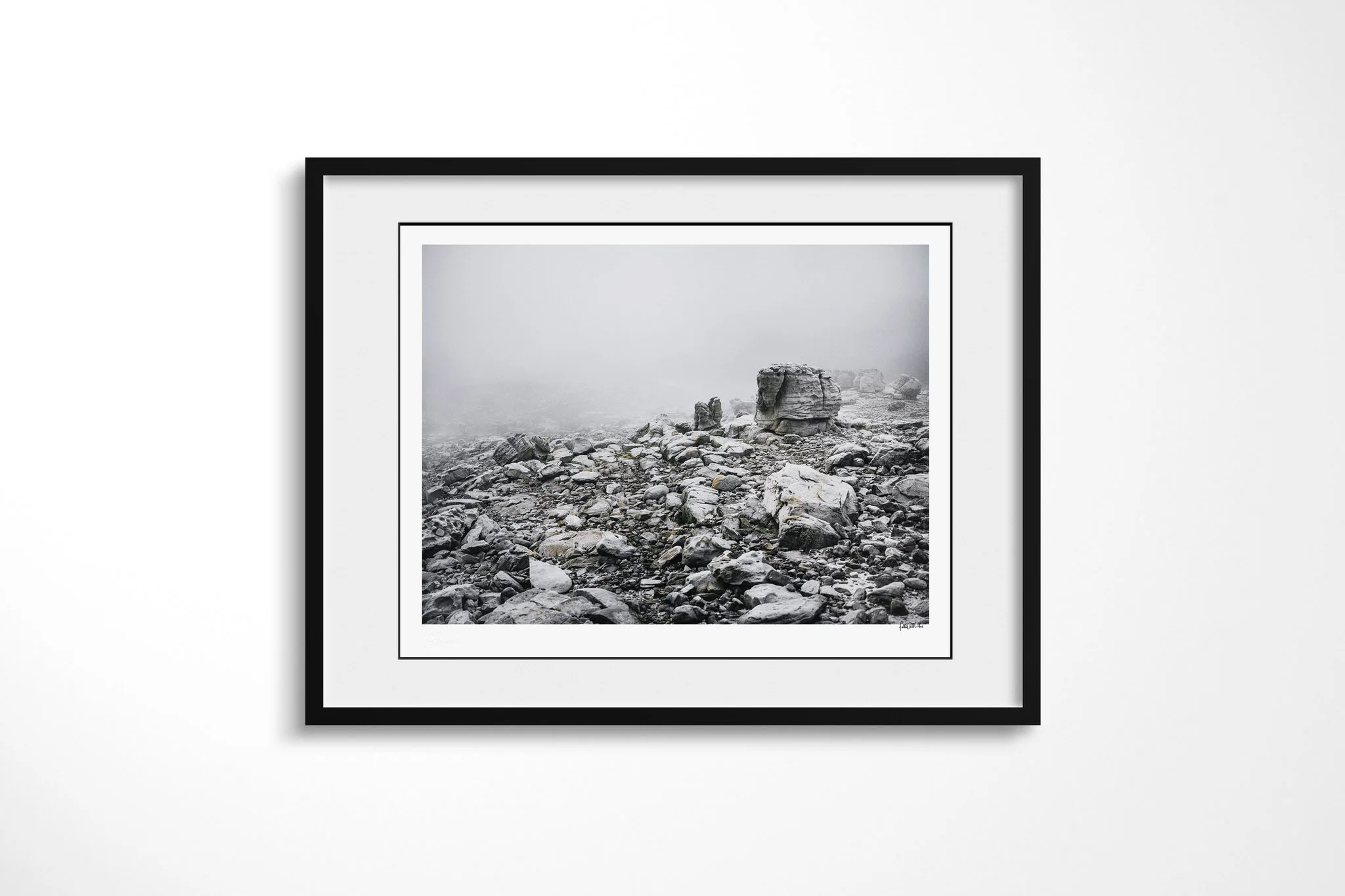 Black-framed fine art print of Atmosphere with a white mount, showing weathered boulders and broken rock fading into dense mist across a pale mountain landscape.