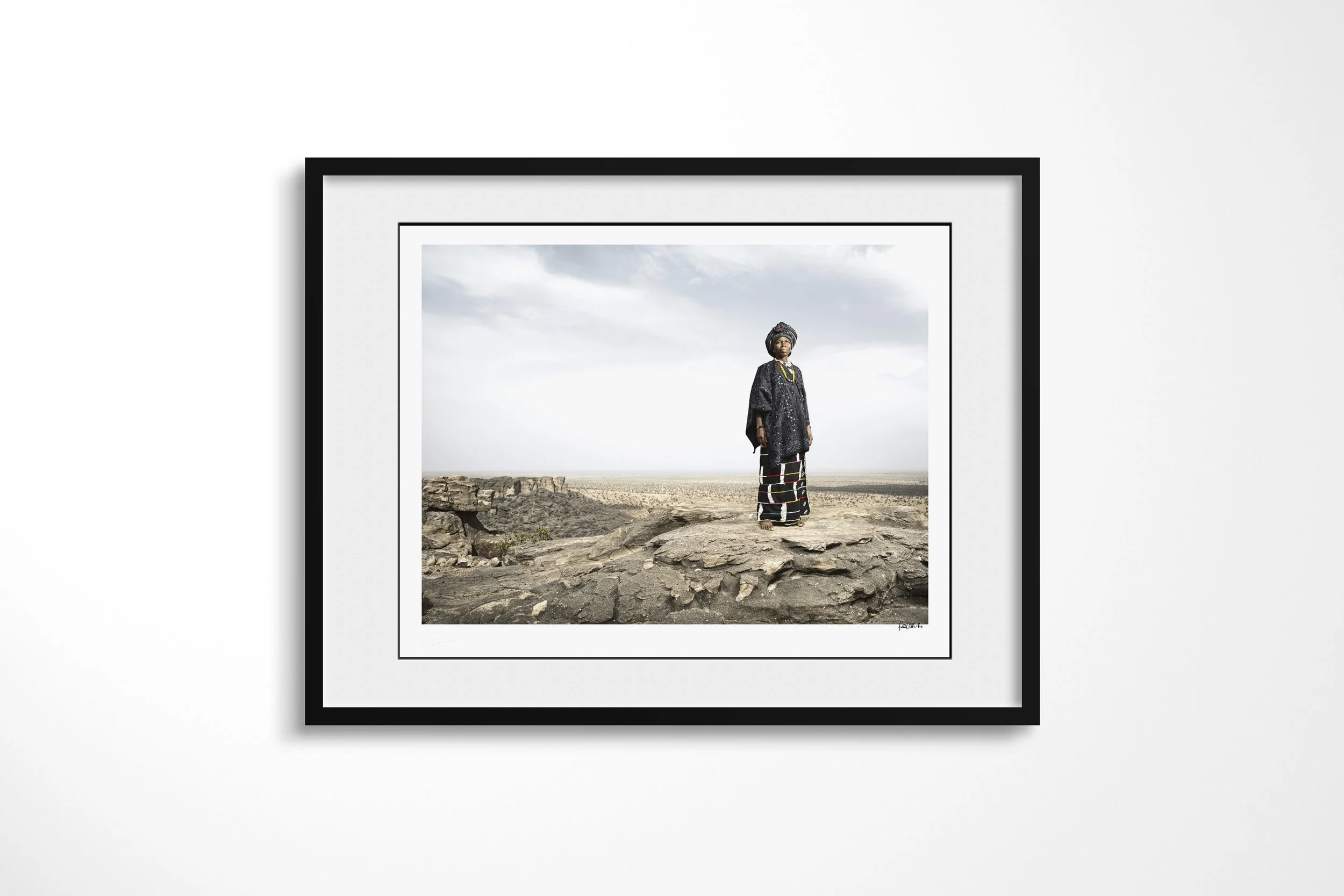 Framed presentation of Timbe in a black frame and white mount, showing Timbe standing on the edge of the Bandiagara Escarpment above the Sahel plain.
