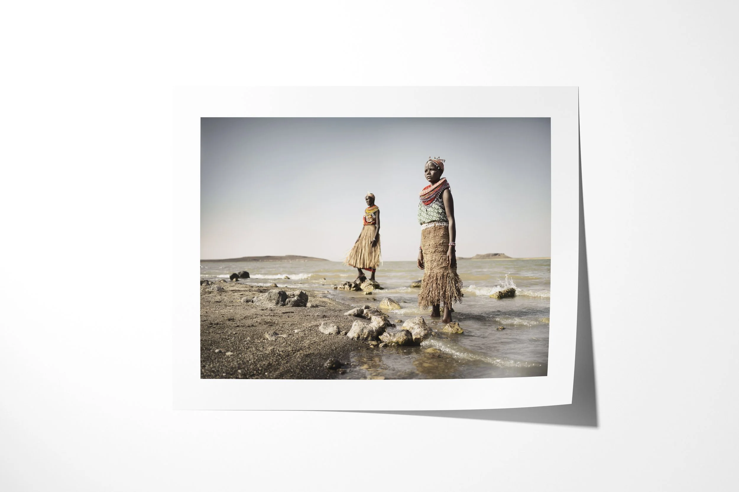 Fine art paper print of Lawra & Nadirie, showing two El Molo women in fibre garments standing on the rocky shore of Lake Turkana.