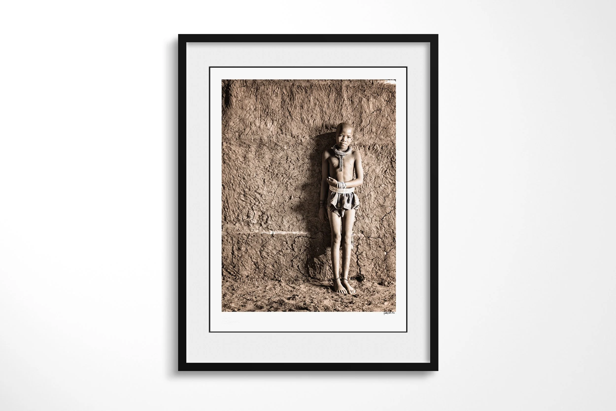 Framed presentation of Potono in a black frame and white mount, showing Potono standing against a textured earthen wall with a child’s close-cropped hairstyle.