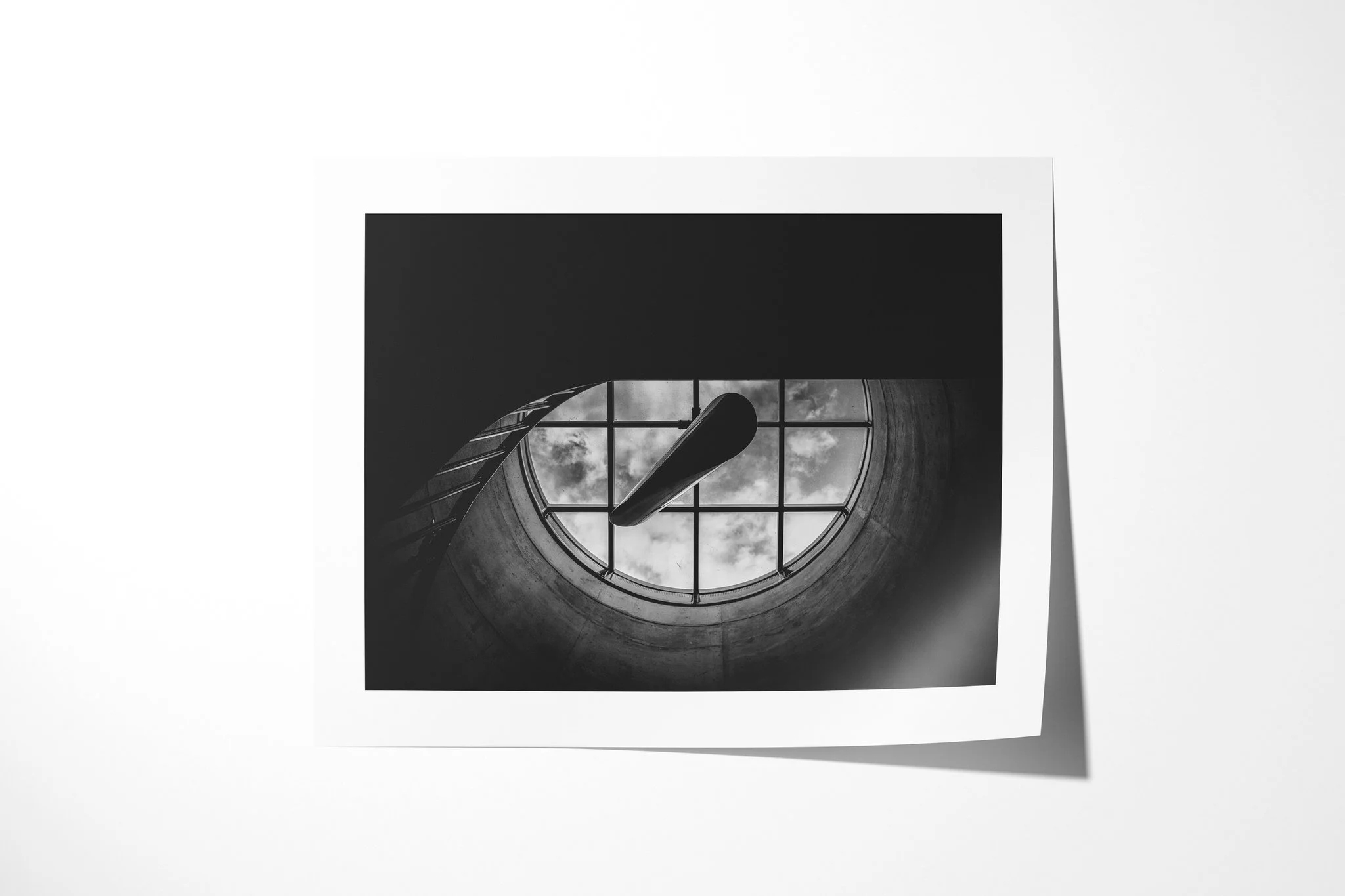 Fine art paper presentation of Skylight, depicting a circular concrete skylight with a window grid and clouds, crossed by two dark blade-like architectural forms.