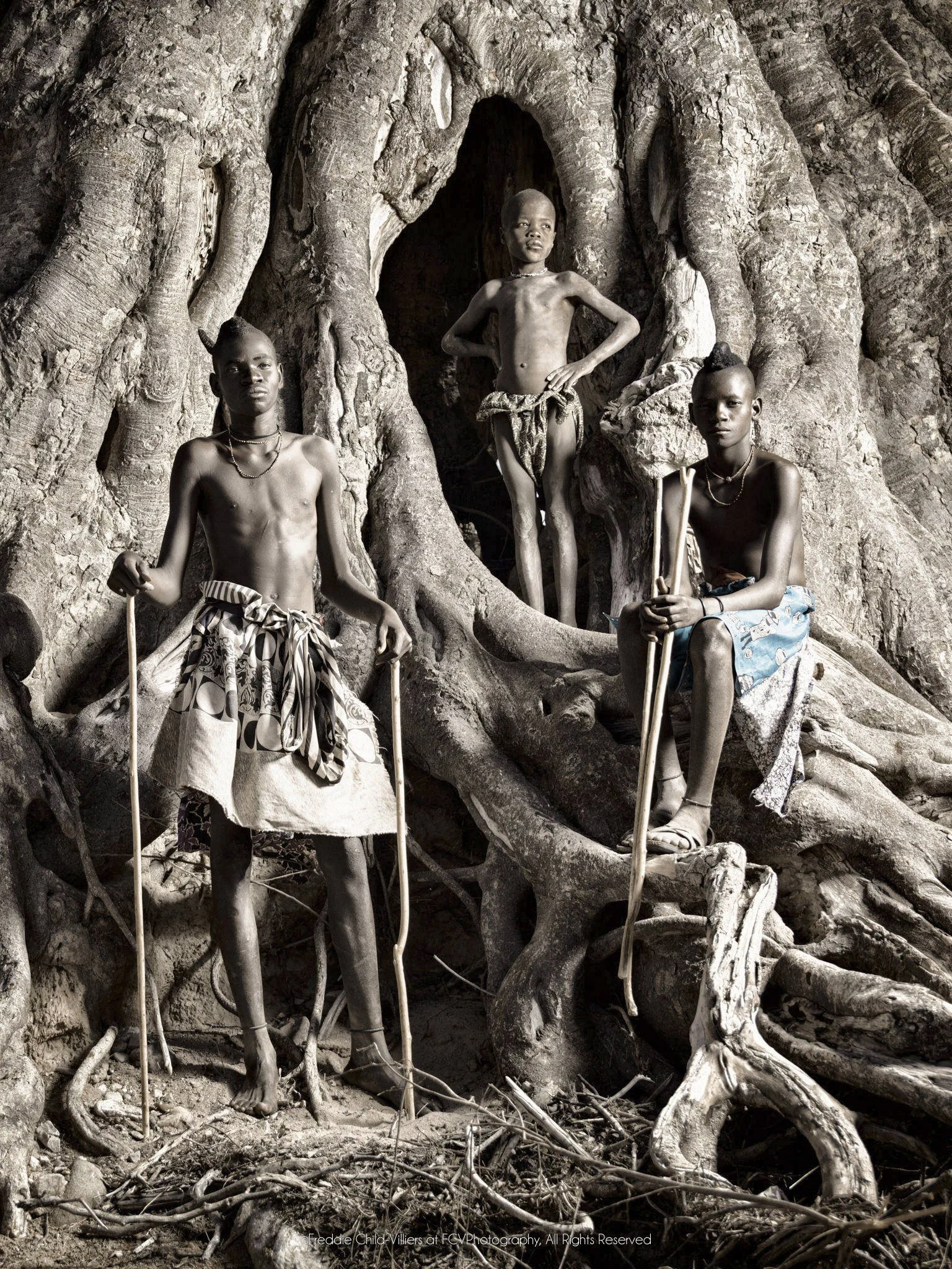 Turimuno (left), Kakoke (middle) and Mbangu (right), three Himba boys standing among the roots and hollows of a monumental fig tree.