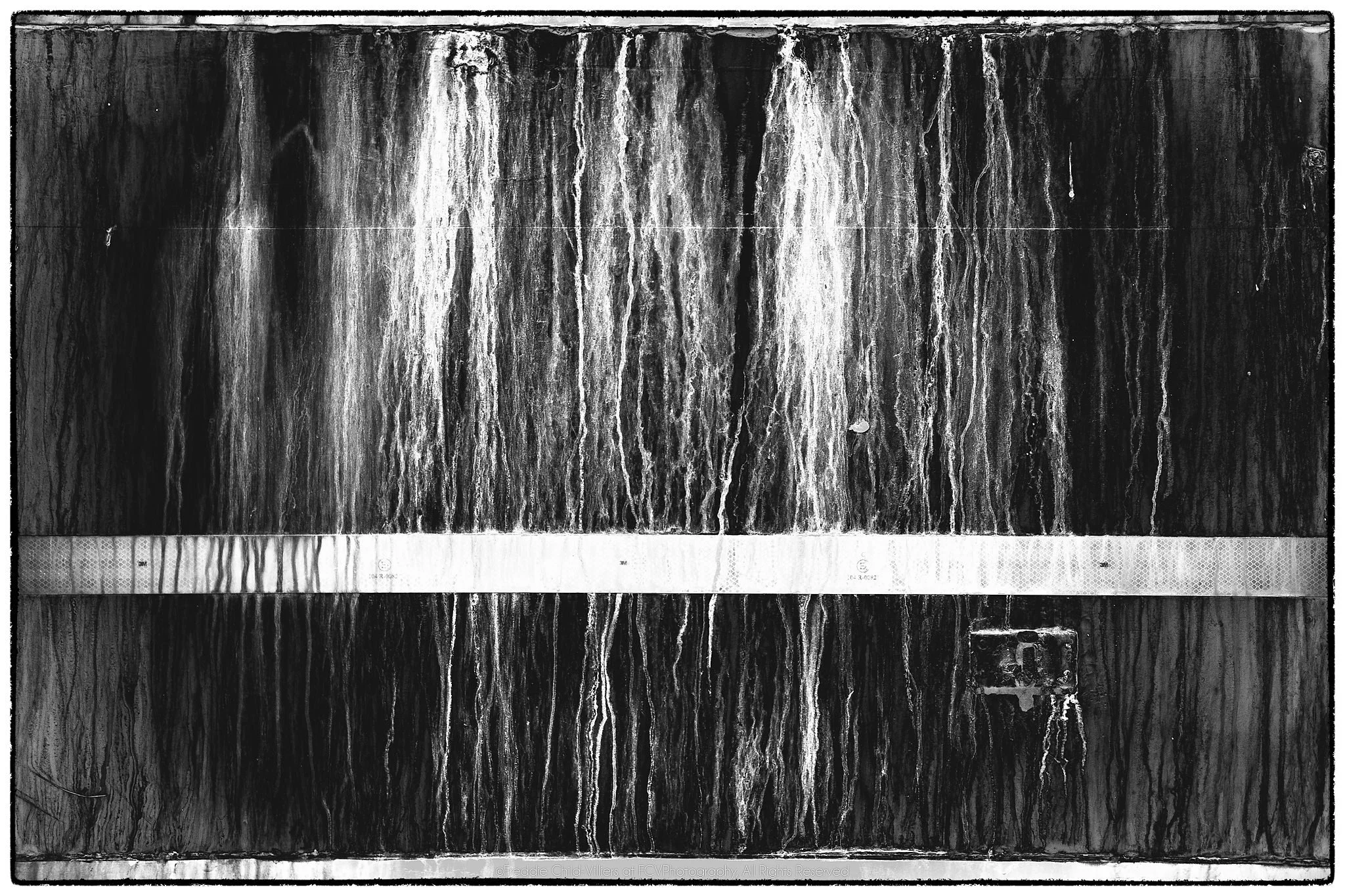 Dark rectangular panel with vertical stains, hard edge lines and a pale horizontal reflective strip.