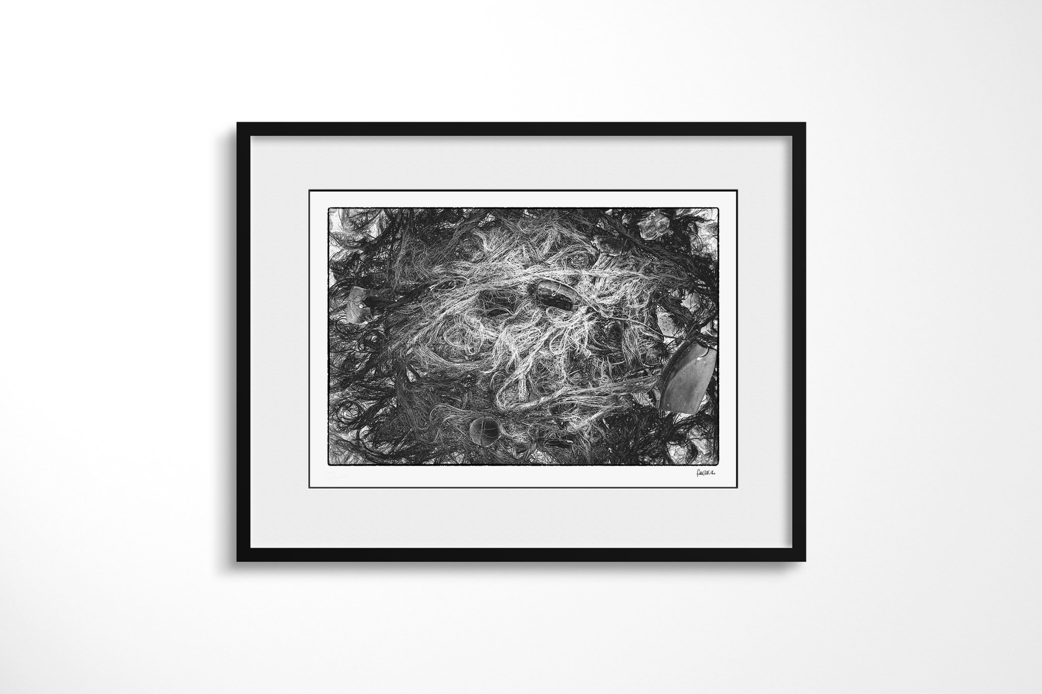 Framed presentation of Tangle in a black frame with a wide white mount, showing a dense tangle of netting, fine cord, rope and scattered weathered fragments in black and white.