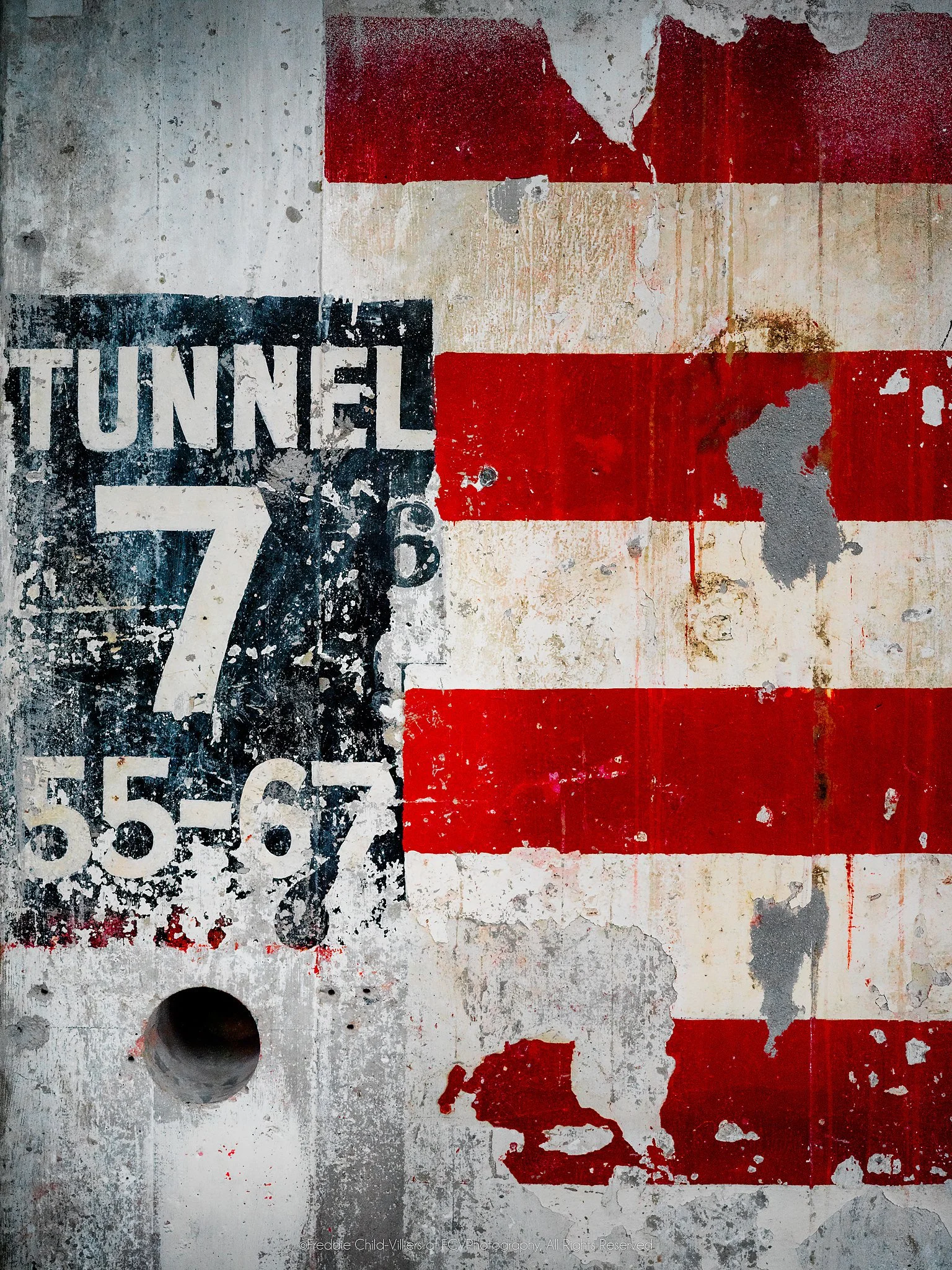 Distressed Tunnel 7 sign beside peeling red-and-white stripes and a circular recess on a weathered industrial wall.