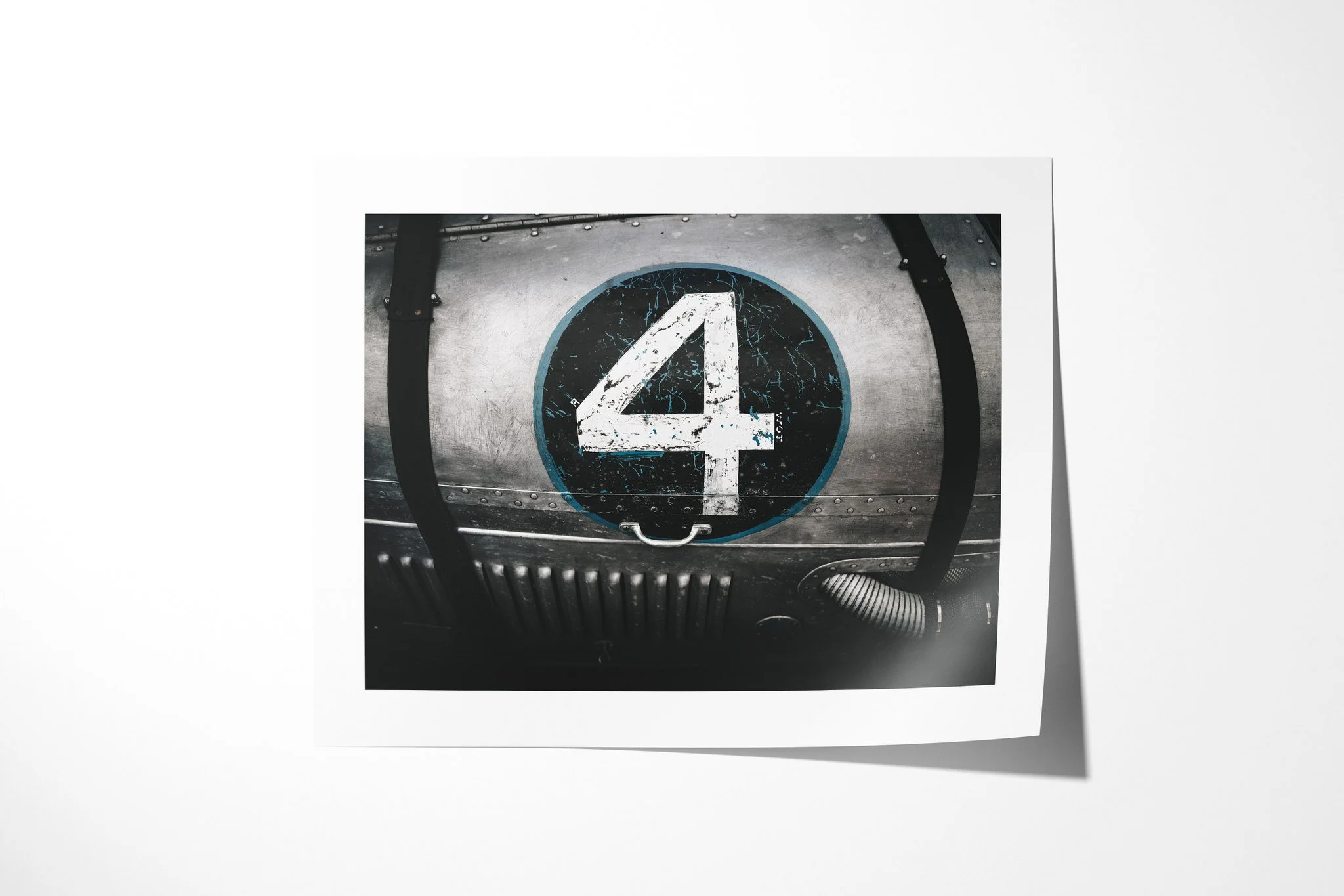 No.4 presented as an unframed fine art paper print, depicting weathered white numeral four on a black circular plate set into riveted metal with straps and ribbed tubing.