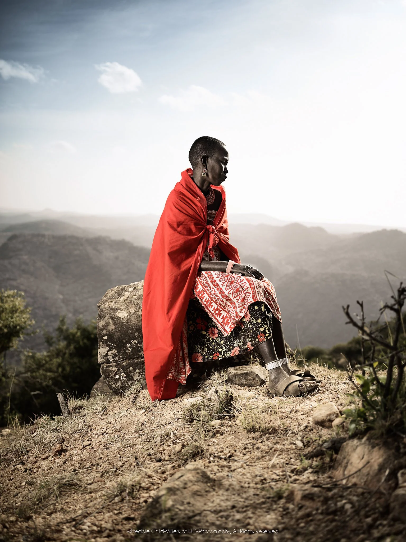 Msari, a Samburu woman in a red wrap seated on a high rock above the Matthews Mountains.