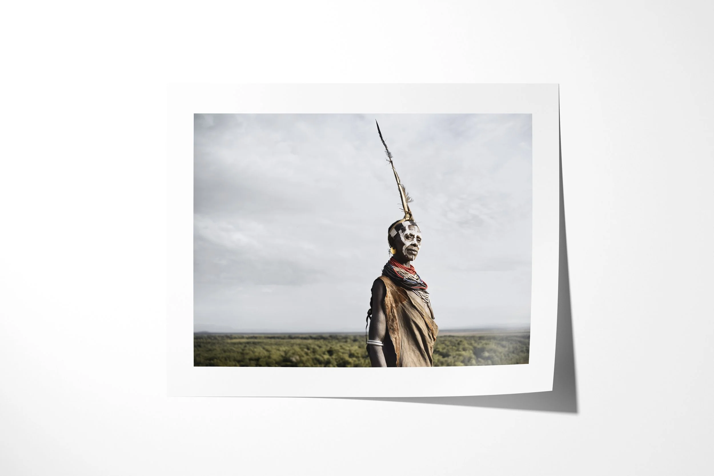 Fine art paper print of Hayla, showing a Kara woman in profile with facial paint, beadwork and a tall feathered headdress above the Omo Valley.