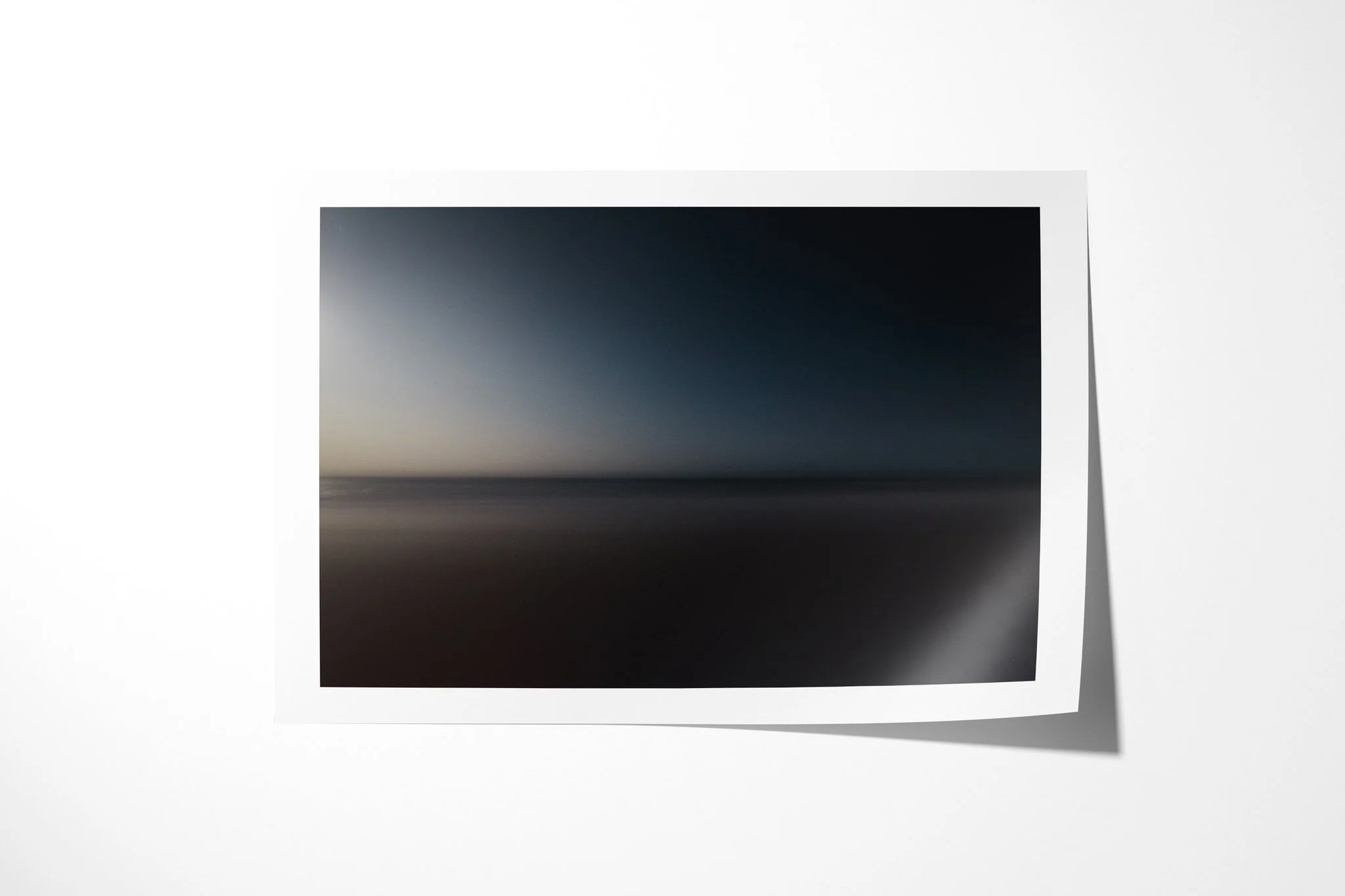 Fine art paper presentation of Outlook, depicting soft, nearly abstract bands of dark blue sky, muted sea and reddish foreground divided by a faint horizon.