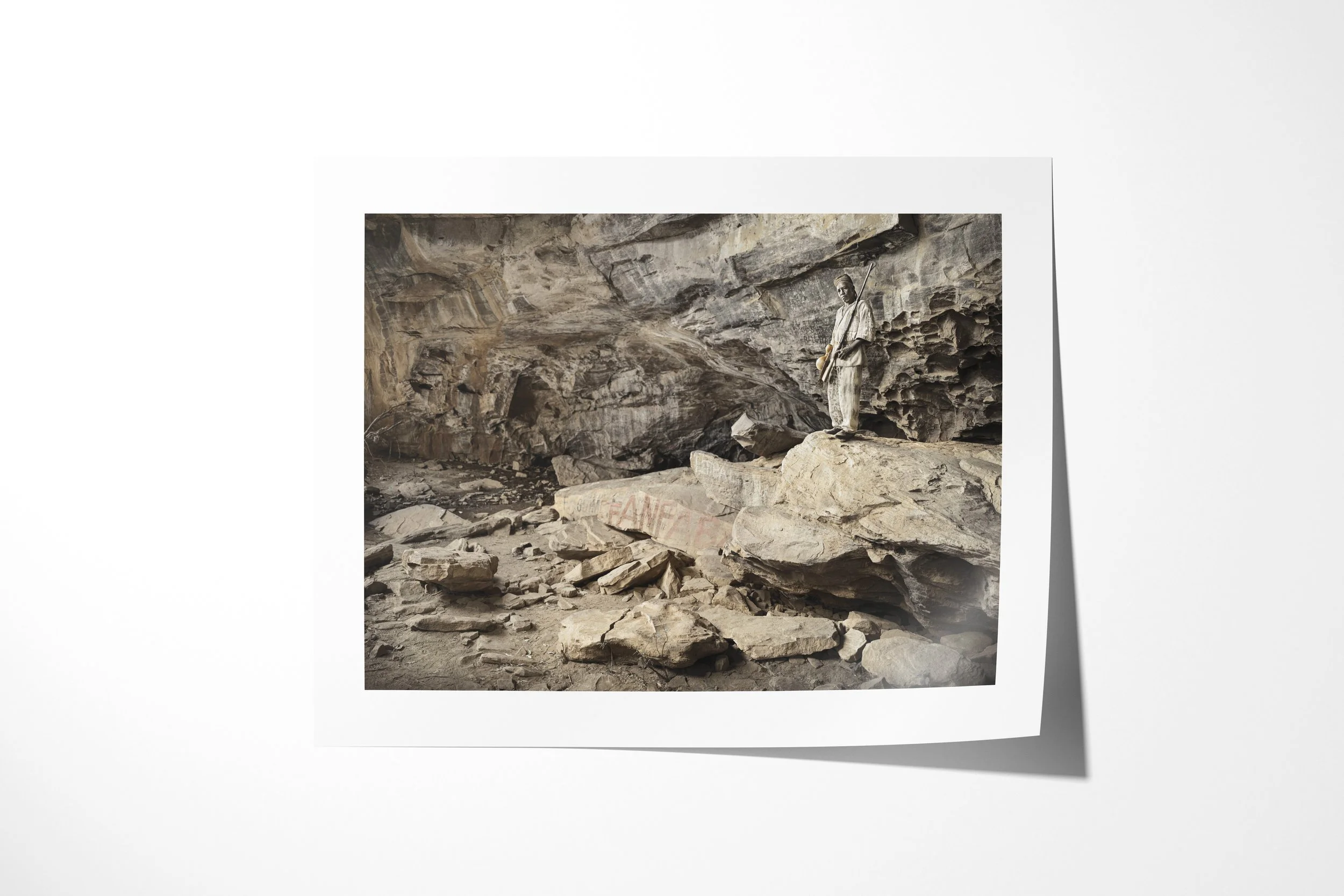 Fine art paper print of Bomary, showing Bomary standing on a rock ledge within the broad chamber of a sacred cave.