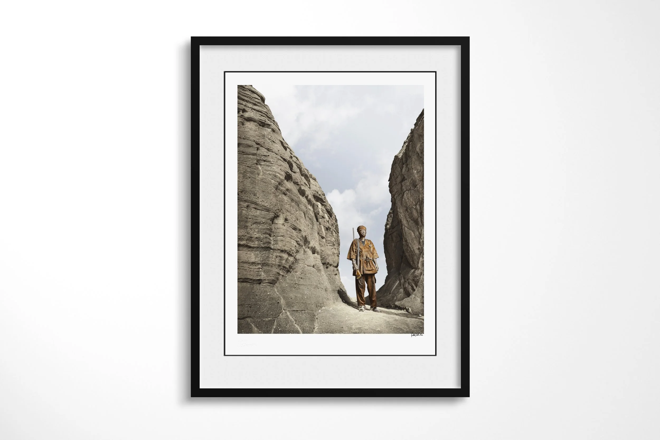 Framed presentation of Jean in a black frame and white mount, showing Jean standing between towering sandstone walls in a narrow mountain passage.