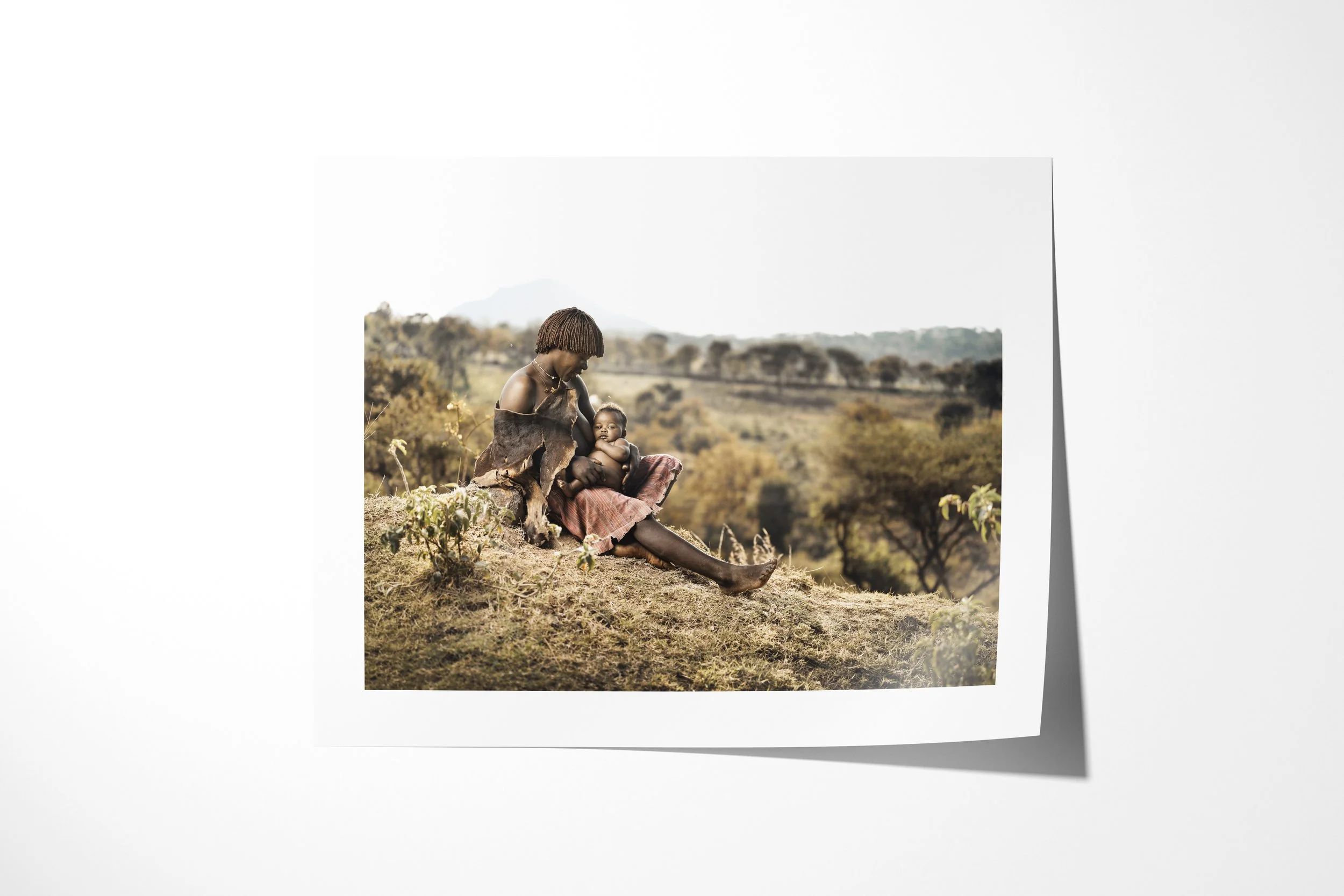 Fine art paper print of Bami & Elsa, showing a Banna mother seated on a hillside holding her young daughter across her lap.