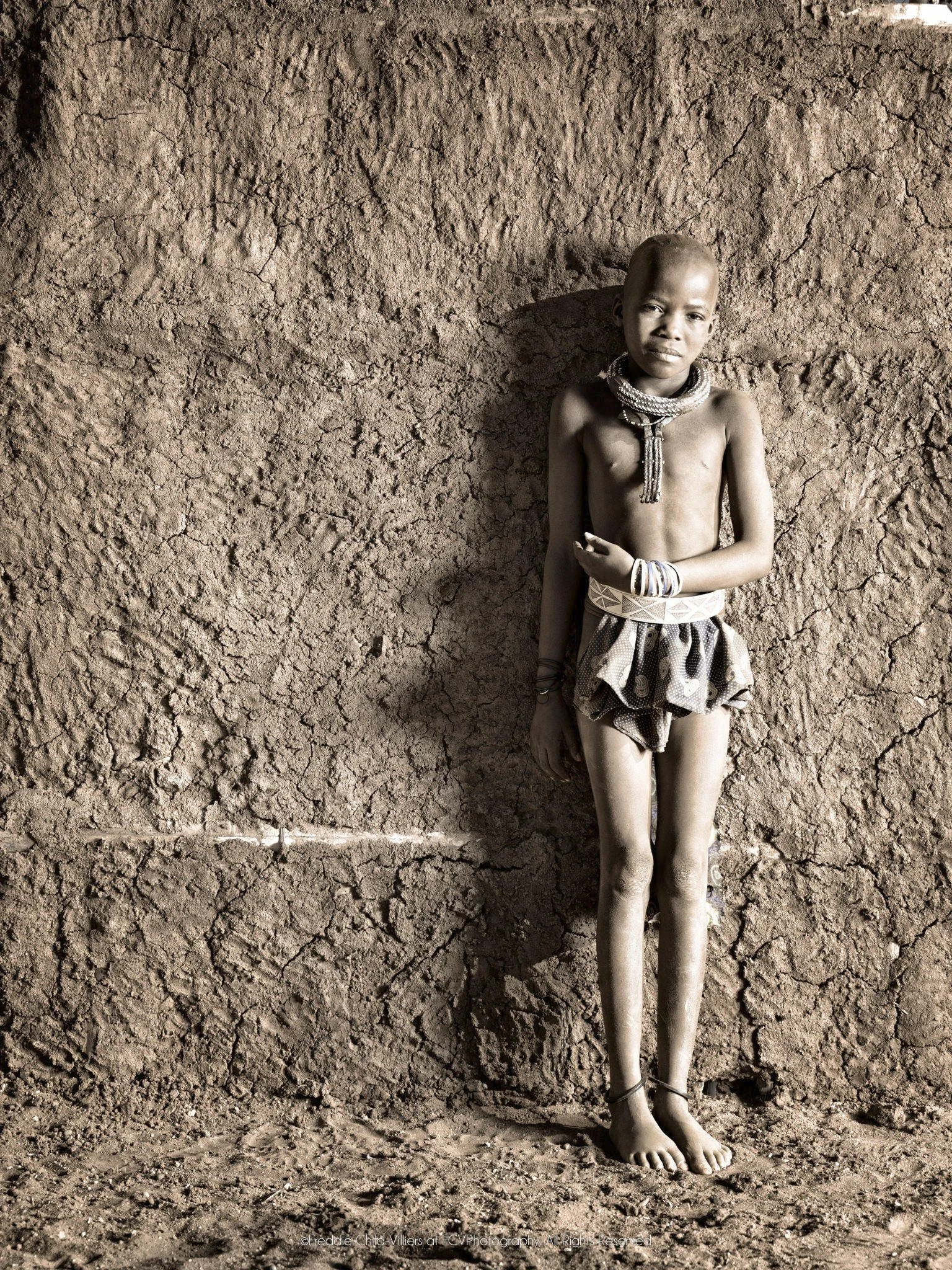 Potono standing against a textured earthen wall with a child’s close-cropped hairstyle.