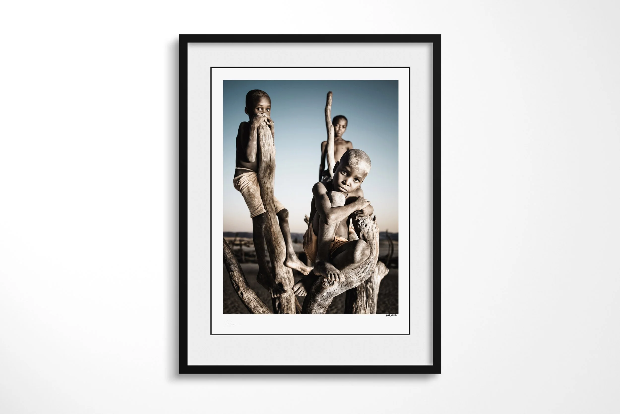 Framed presentation of Turimuje and friends in a black frame and white mount, showing three Himba boys gathered closely on the branches of a leafless tree.